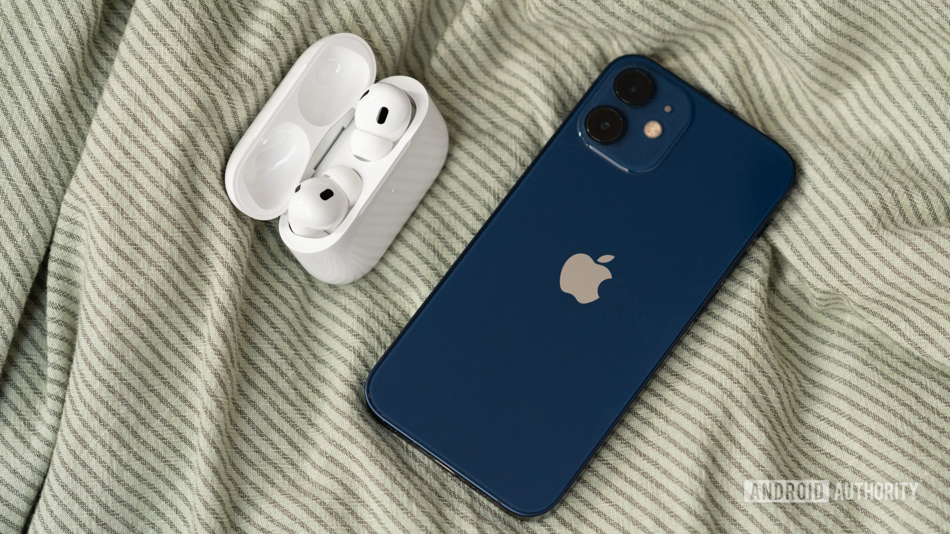 The Apple AirPods Pro (2nd generation) case open with the earbuds next to an iPhone 12 mini.