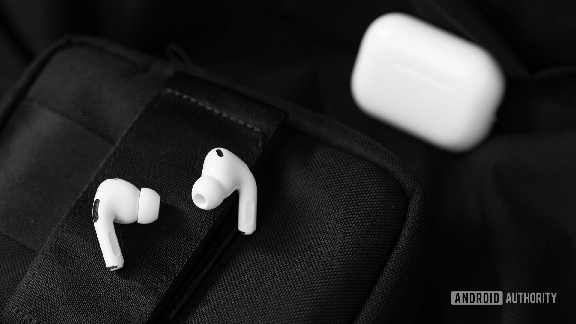 The Apple AirPods Pro (2nd generation) earbuds rest on a black surface with the case in the background.