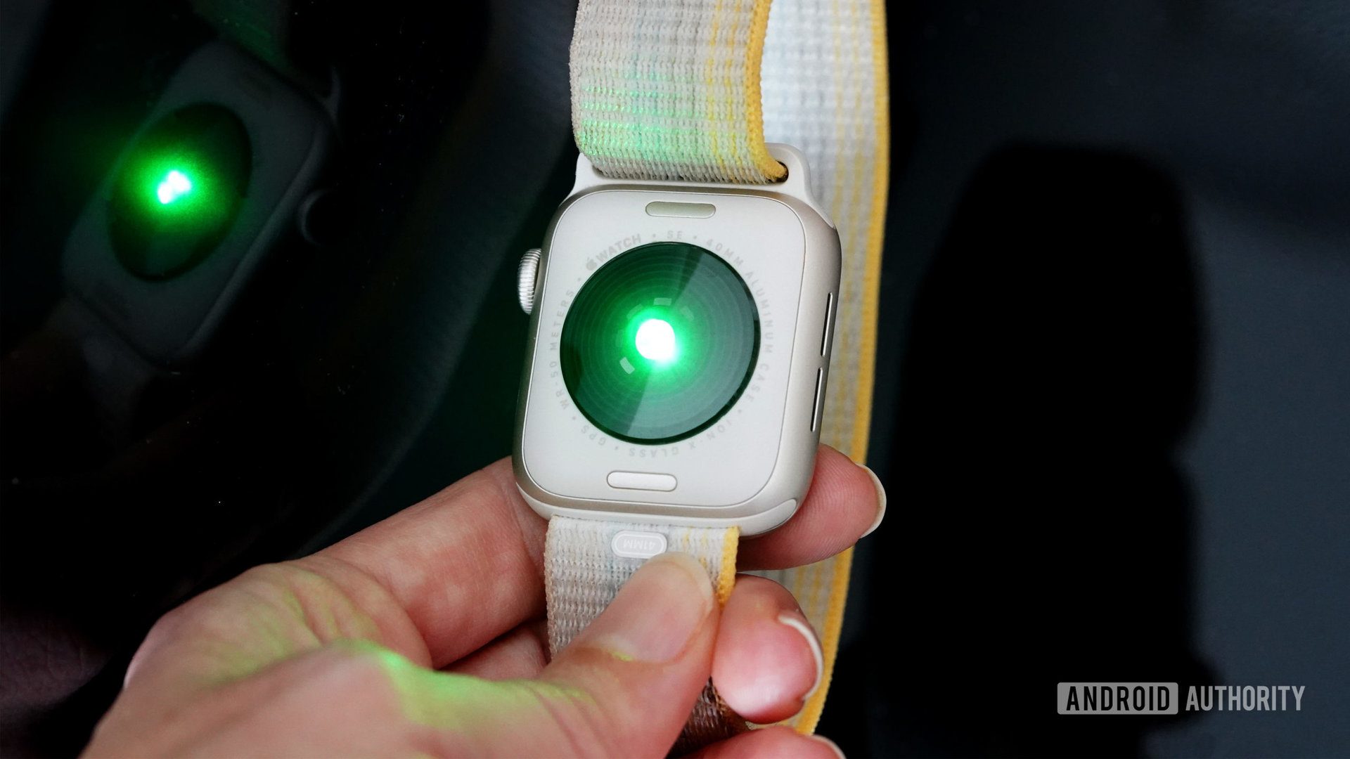 An Apple Watch SE 2 holds the device face down, displaying the heart rate LED lights.
