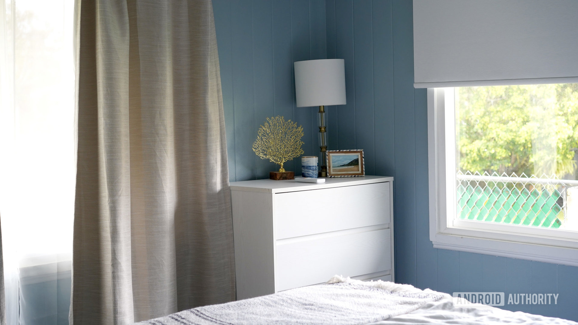 A small bedroom utilizes a smart blind on one wall and traditional curtains on another.