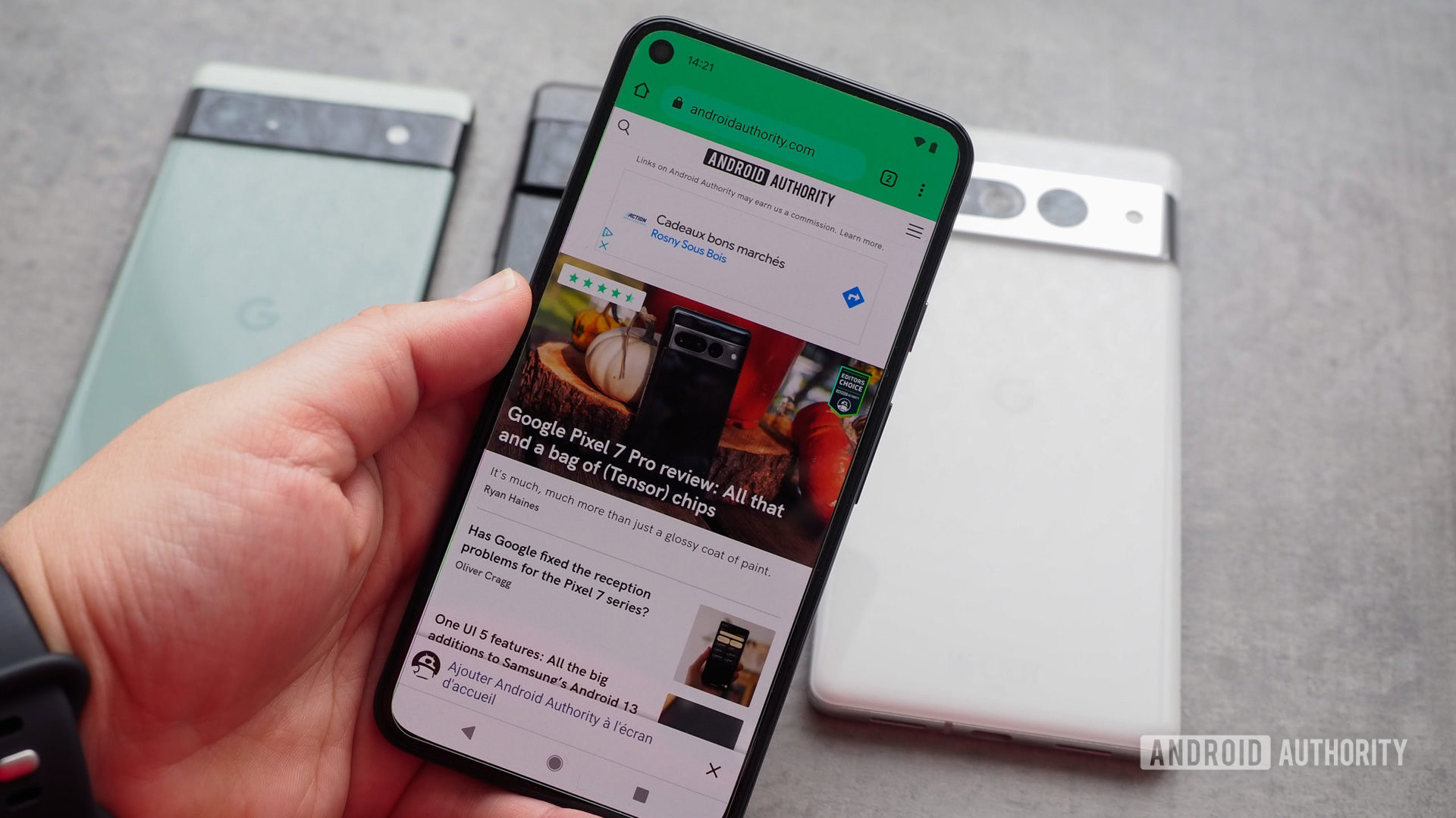 Google Pixel 5 in hand with the display on, showing the Android Authority website, with several Pixels behind it on the table