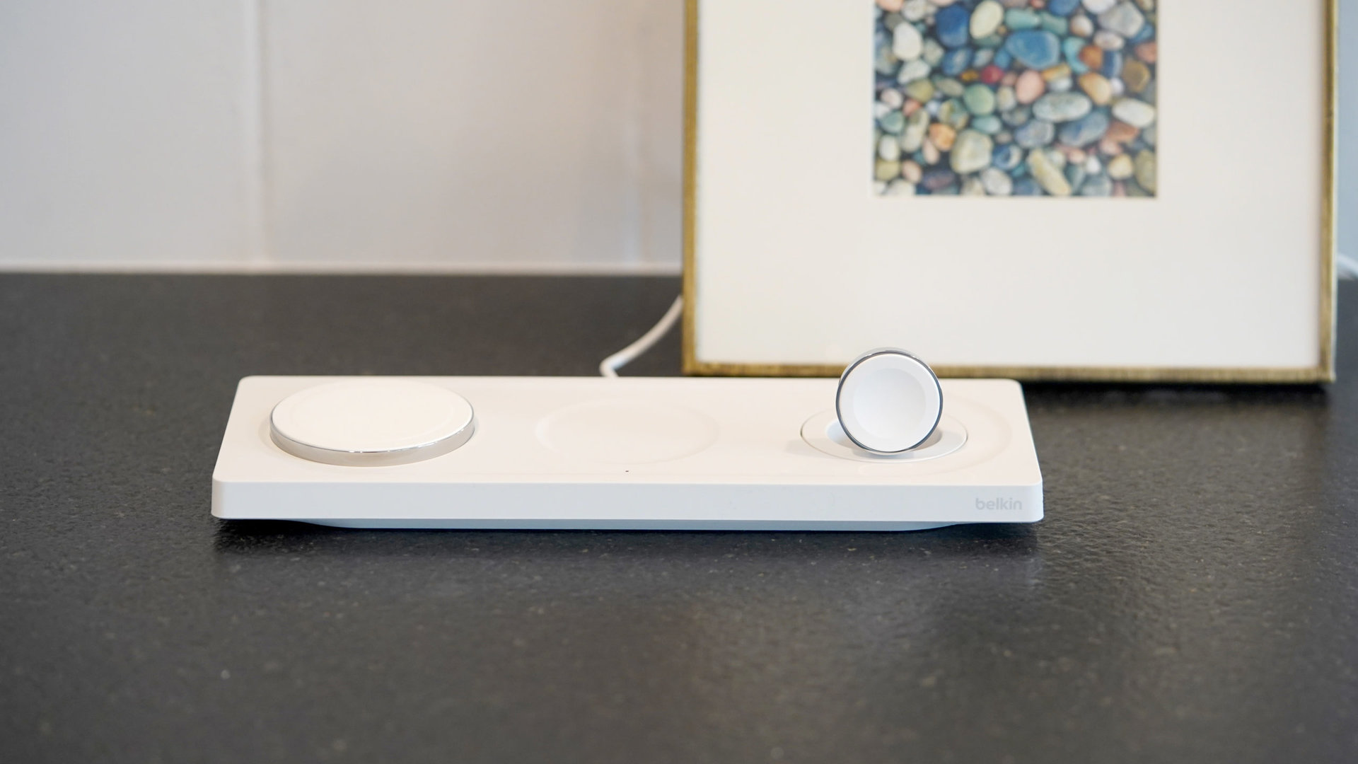 A Belkin BoostCharge Pro 3-in-1 Wireless Charging Pad rests on a black countertop.
