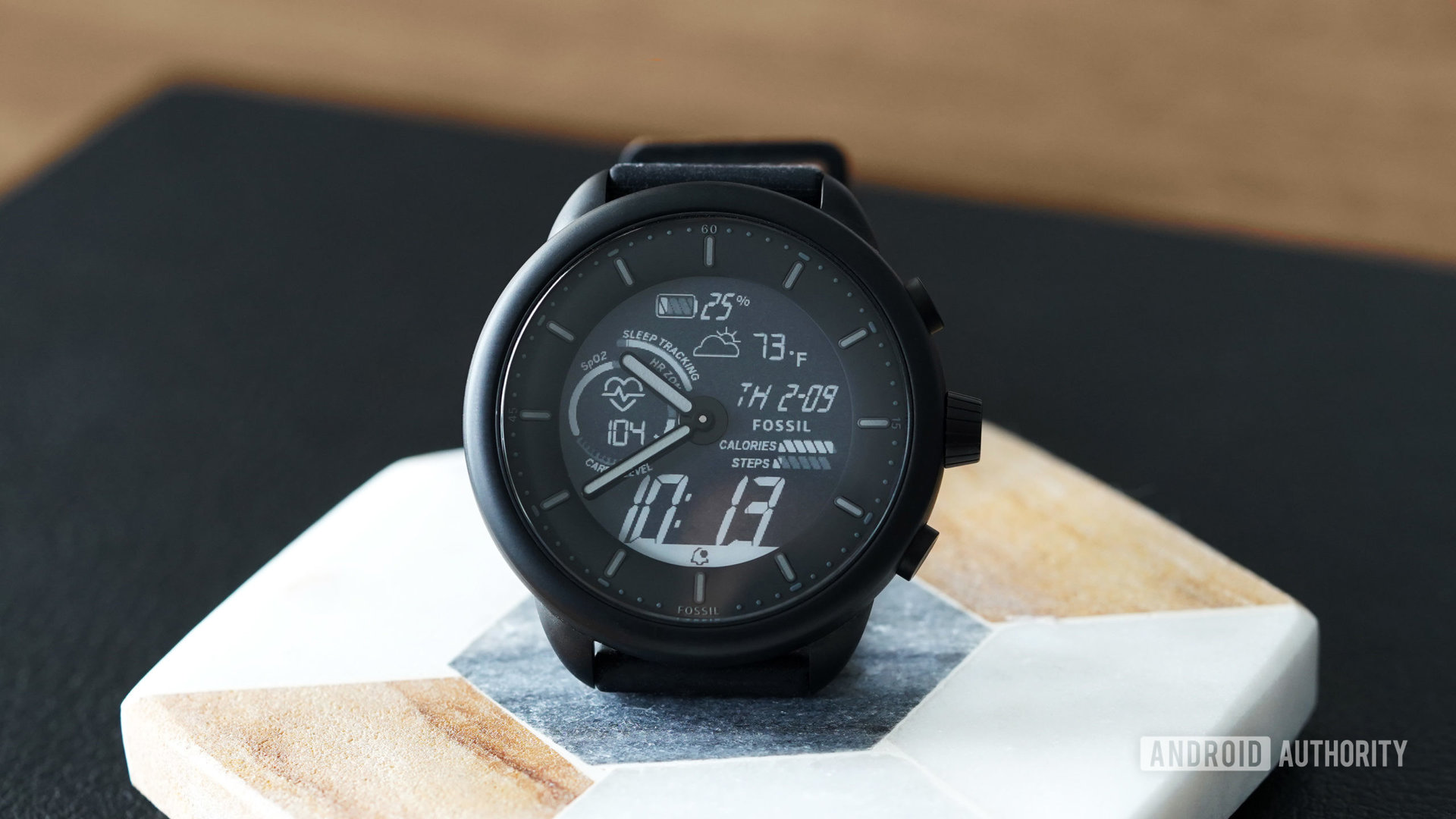 A Fossil Gen 6 Hybrid Wellness Edition displays the Wellness Dark watch face.