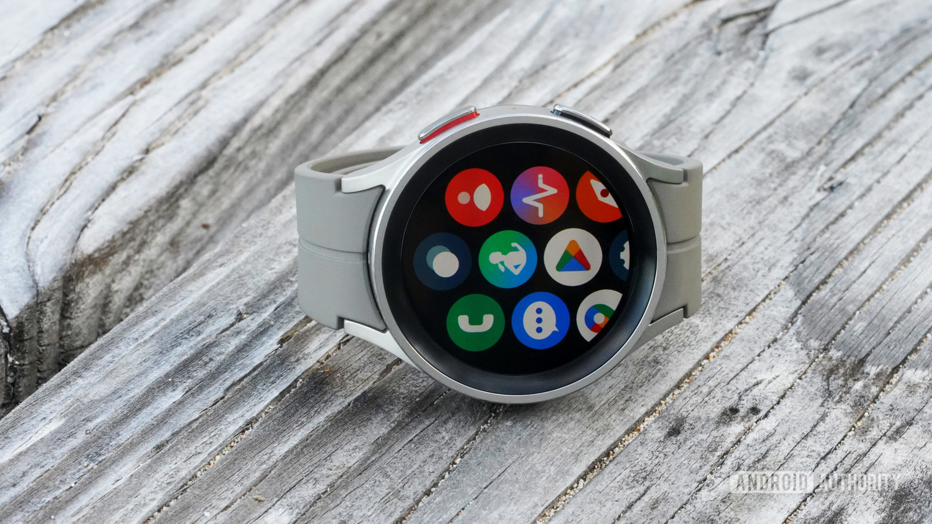 A Galaxy Watch 5 Pro rests on picnic table displays its app library.