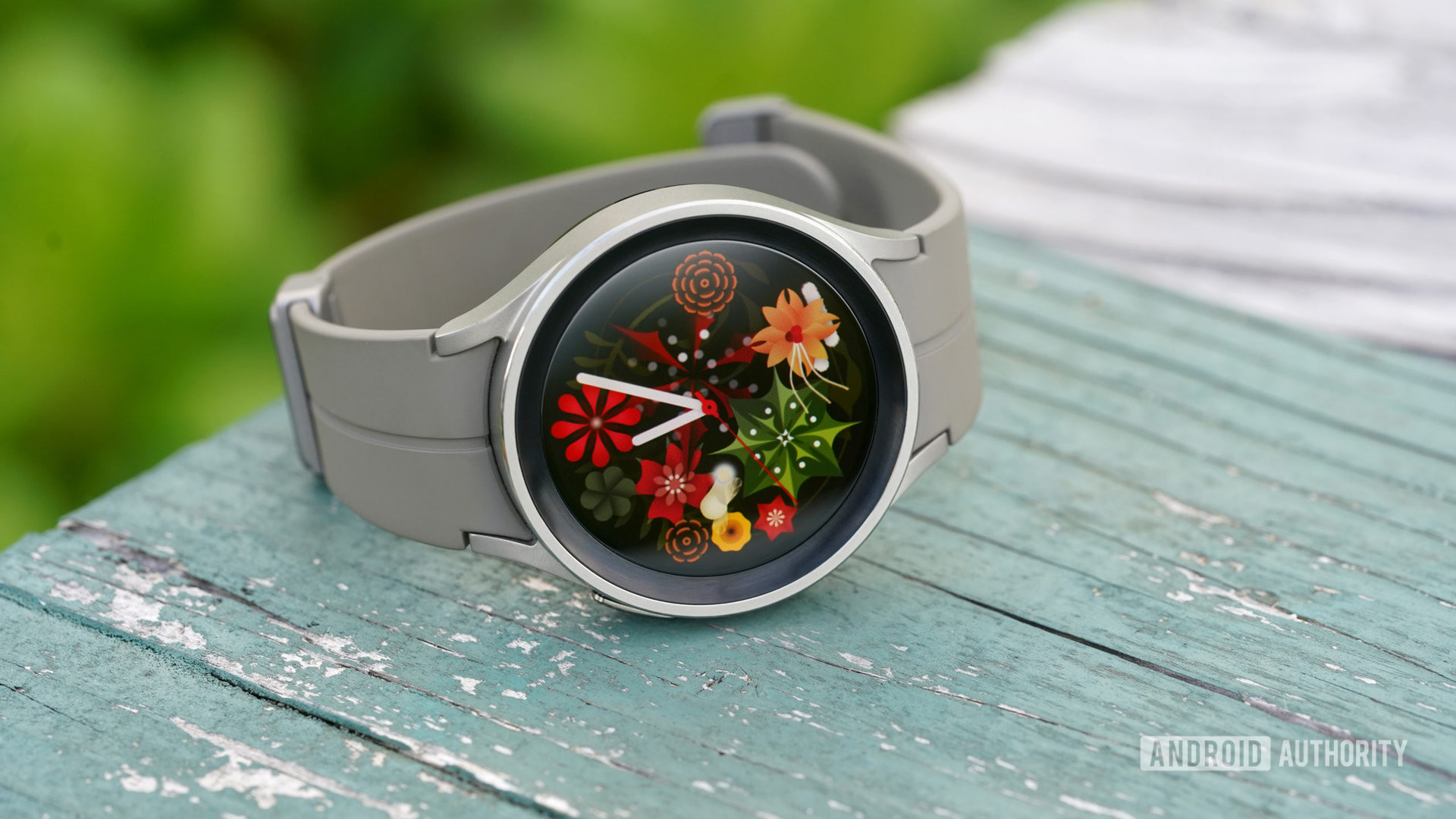 A Galaxy Watch 5 Pro rests on a table displaying the Flower Garden watch face.