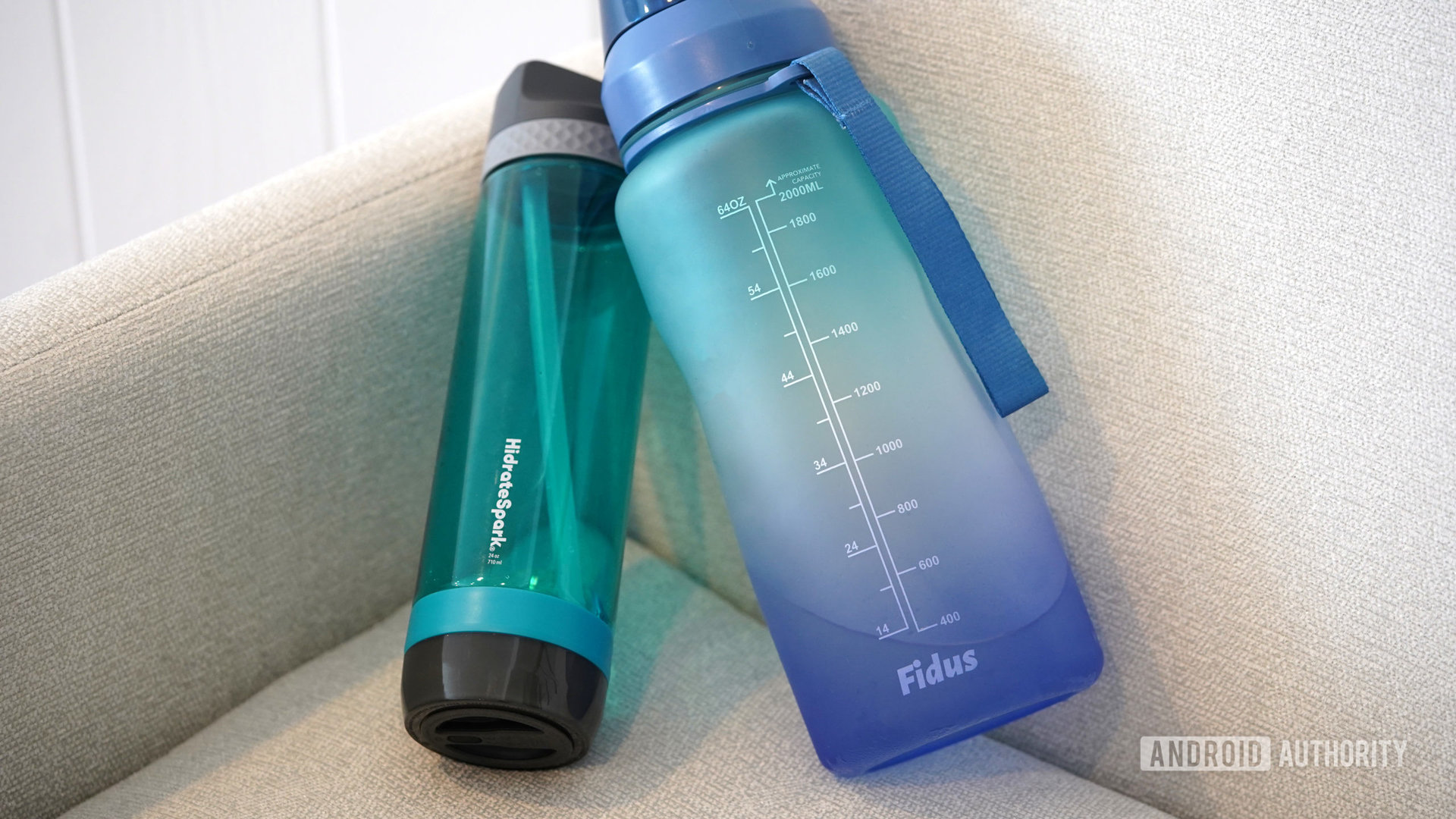 A HidrateSpark Pro Lite rests on a chair alongside a bottle without smart features.