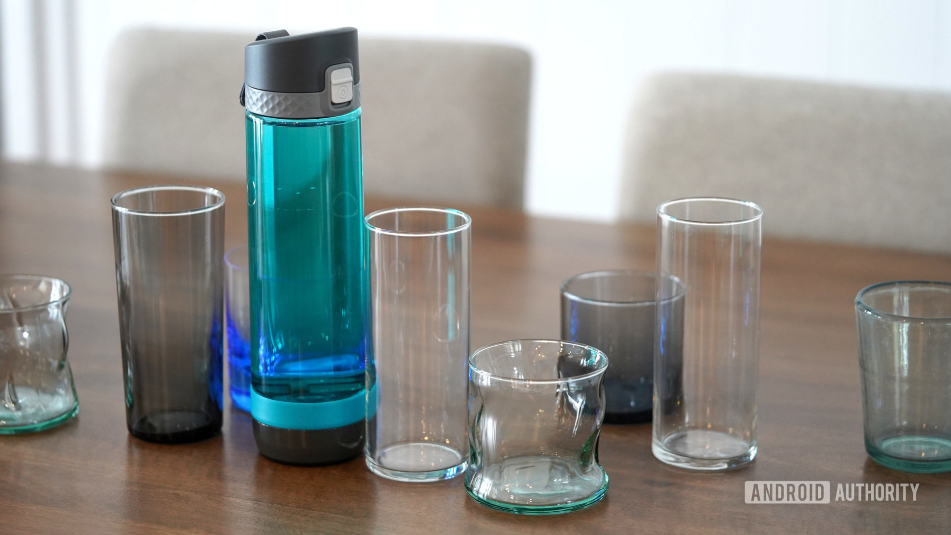 A smart water bottle stands among empty water glasses.