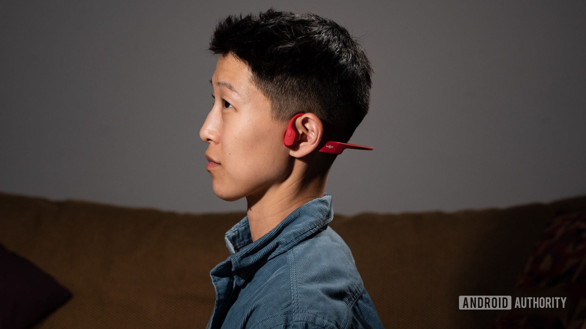 A person wears the Shokz OpenRun bone conduction open ear headphones in red.