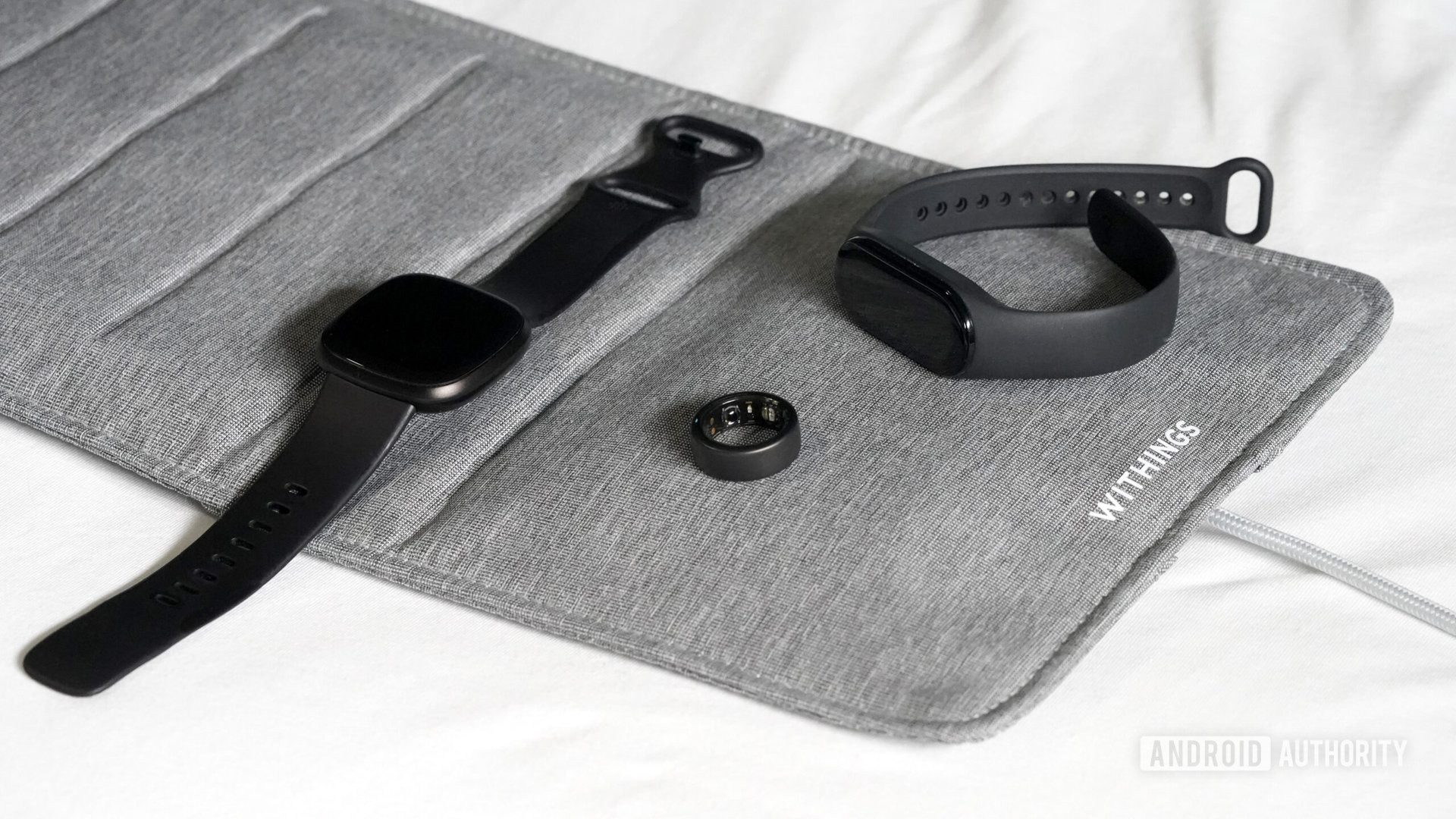 A variety of the best sleep trackers available rest on a bed.