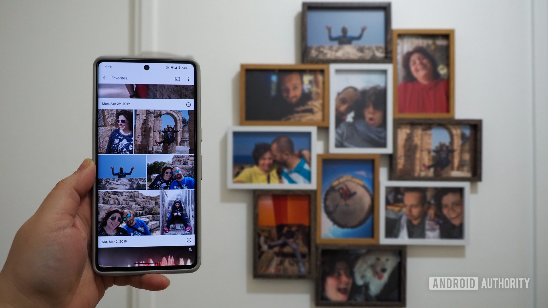 Hand holding a Pixel 7 Pro with Google Photos favorites grid, with a photo frame in the background that has Google Photos prints