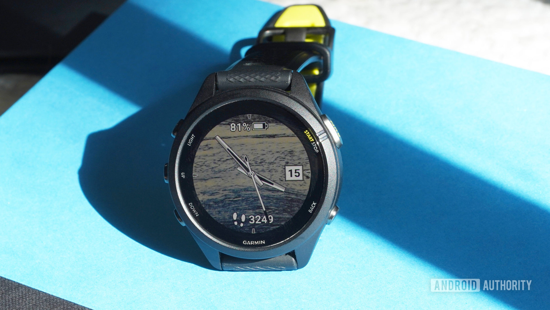A Garmin Forerunner 265S perches on a blue book, displaying a users personal photo as a watch face.