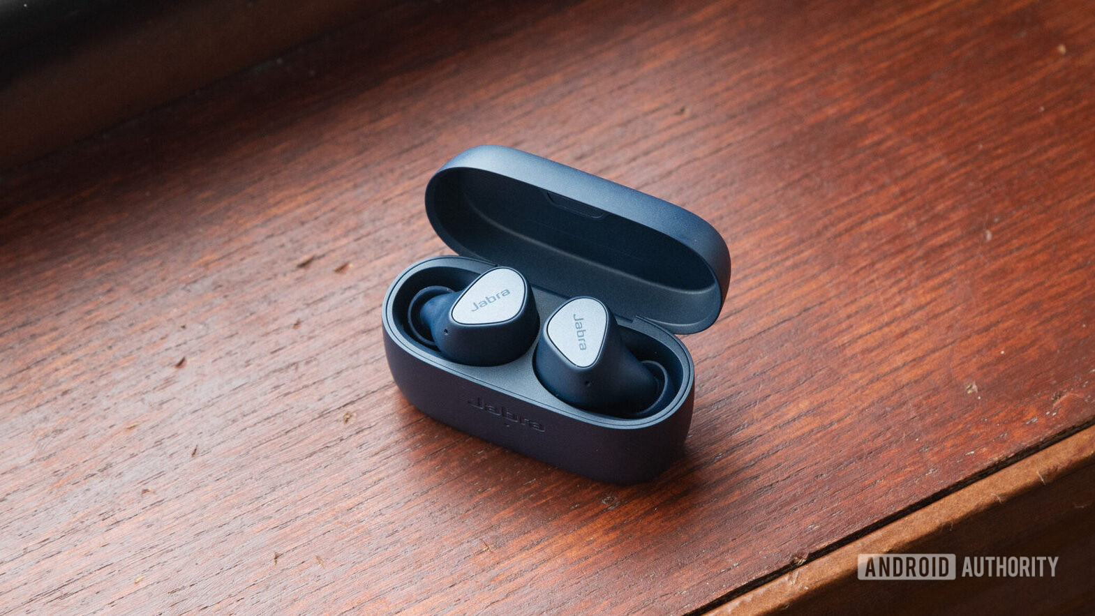 The Jabra Elite 4 wireless noise-cancelling earbuds in the open case on a wooden surface.