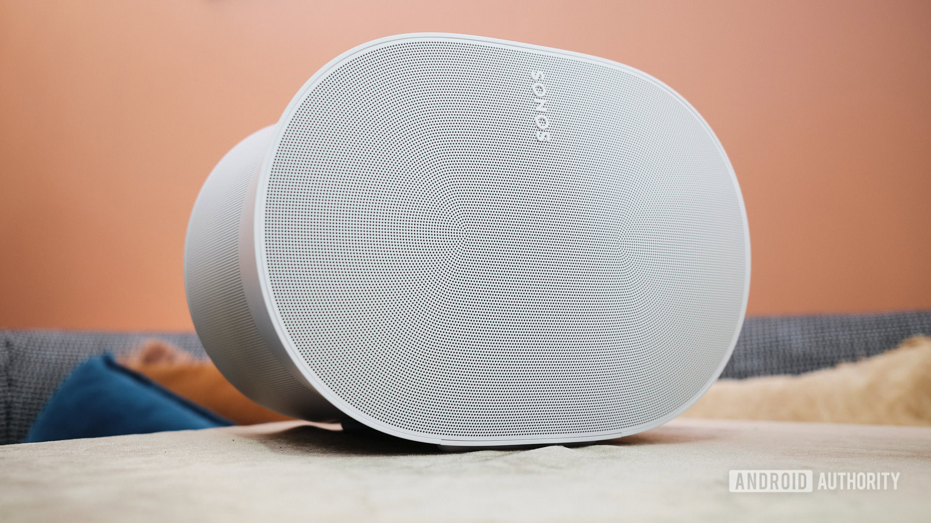 The Sonos Era 300 smart speaker on a table in front of an orange wall.