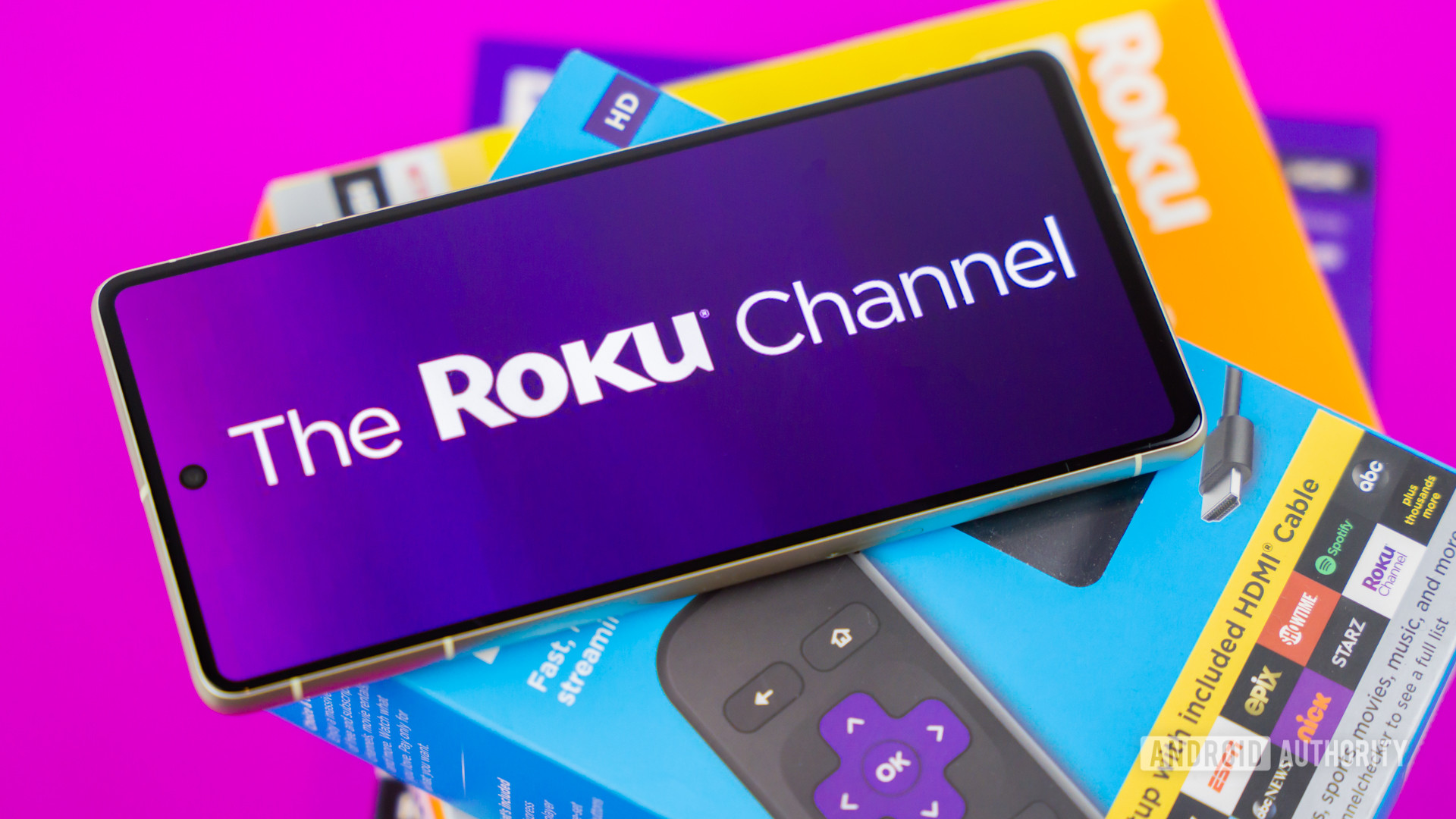 Stock photo of The Roku Channel logo on phone next to Roku boxes 7