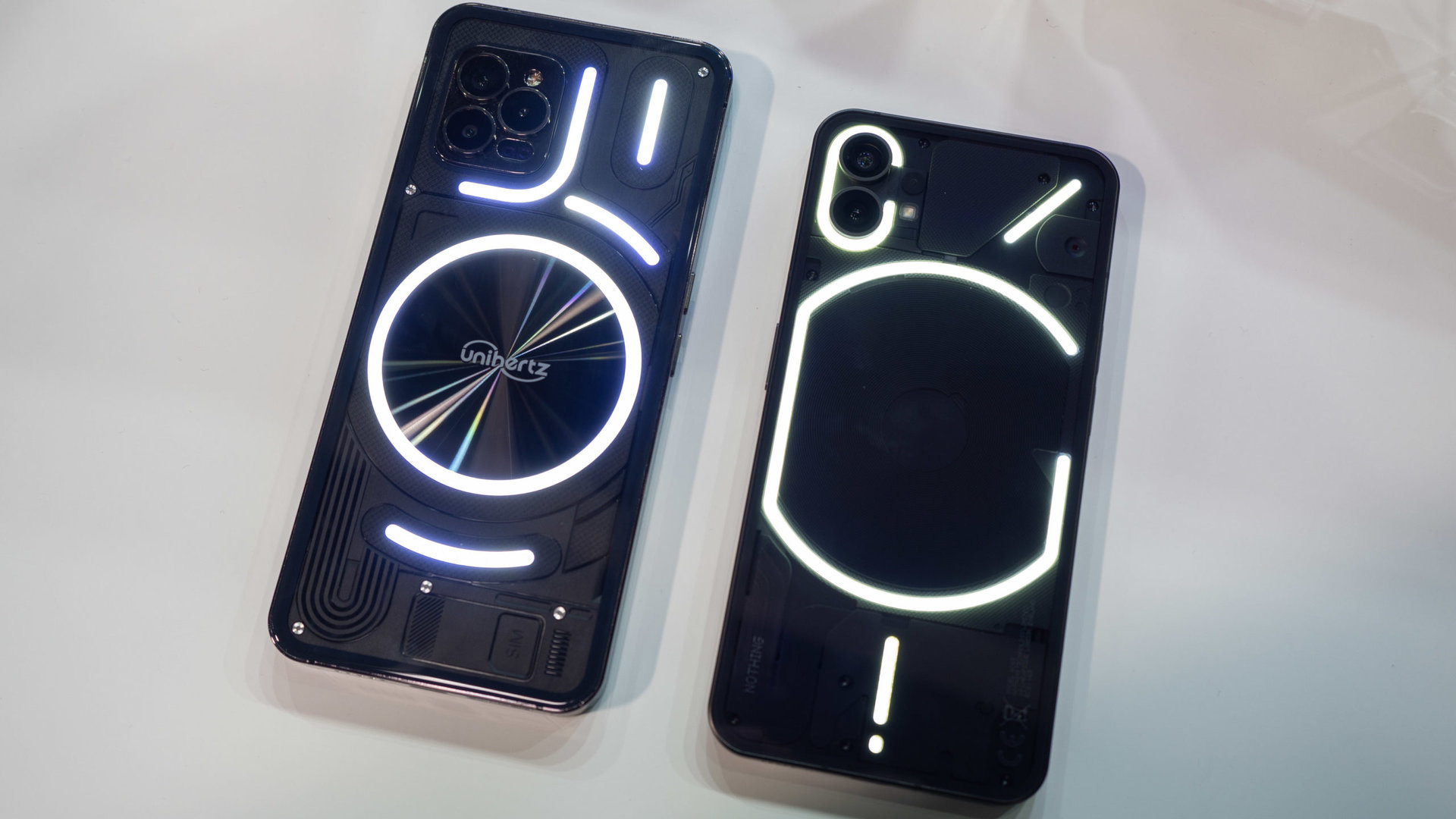 Black Unihertz Luna phone, from the back, with white lights, next to a Nothing Phone 1