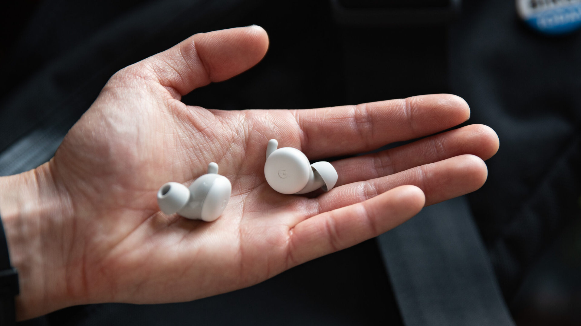 A hand holds the Google Pixel Buds A-Series earbuds.