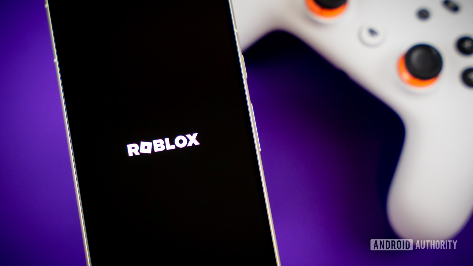 Roblox game logo on smartphone next to controller Stock photo 1
