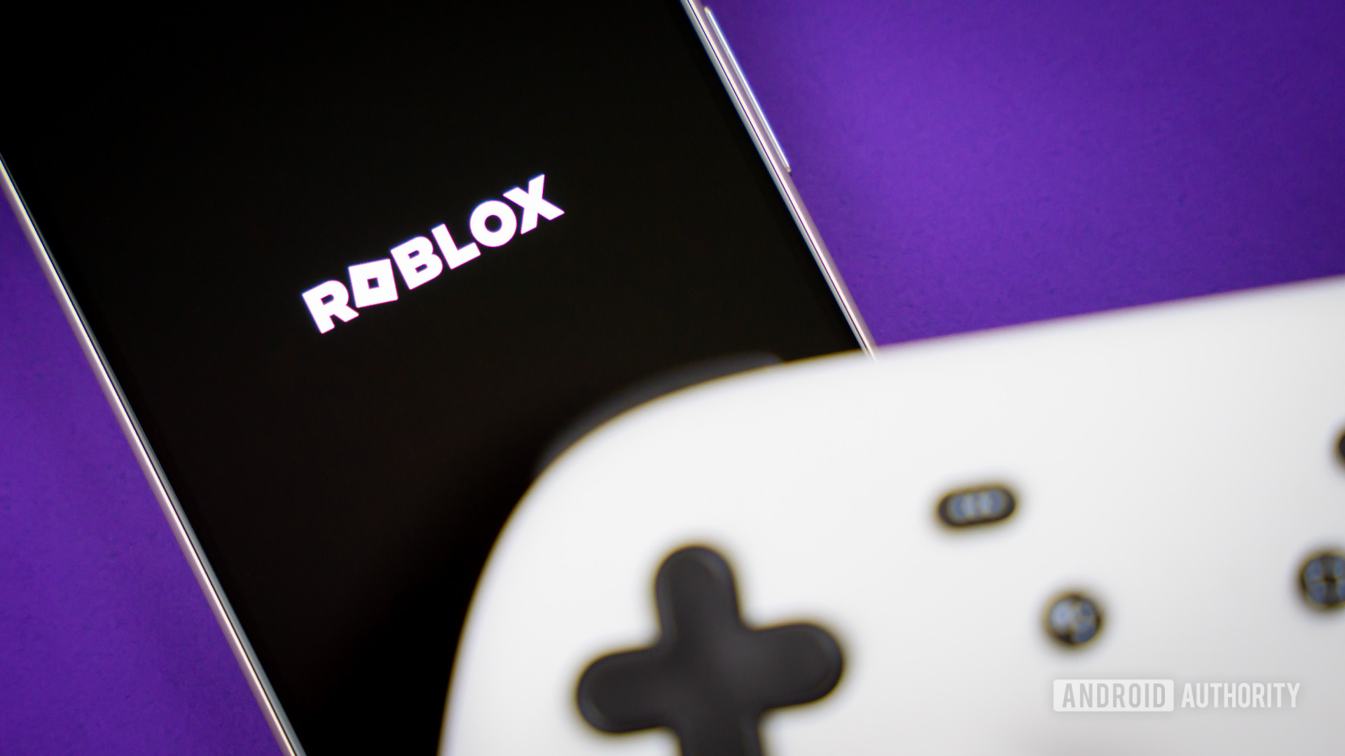 Roblox game logo on smartphone next to controller Stock photo 3
