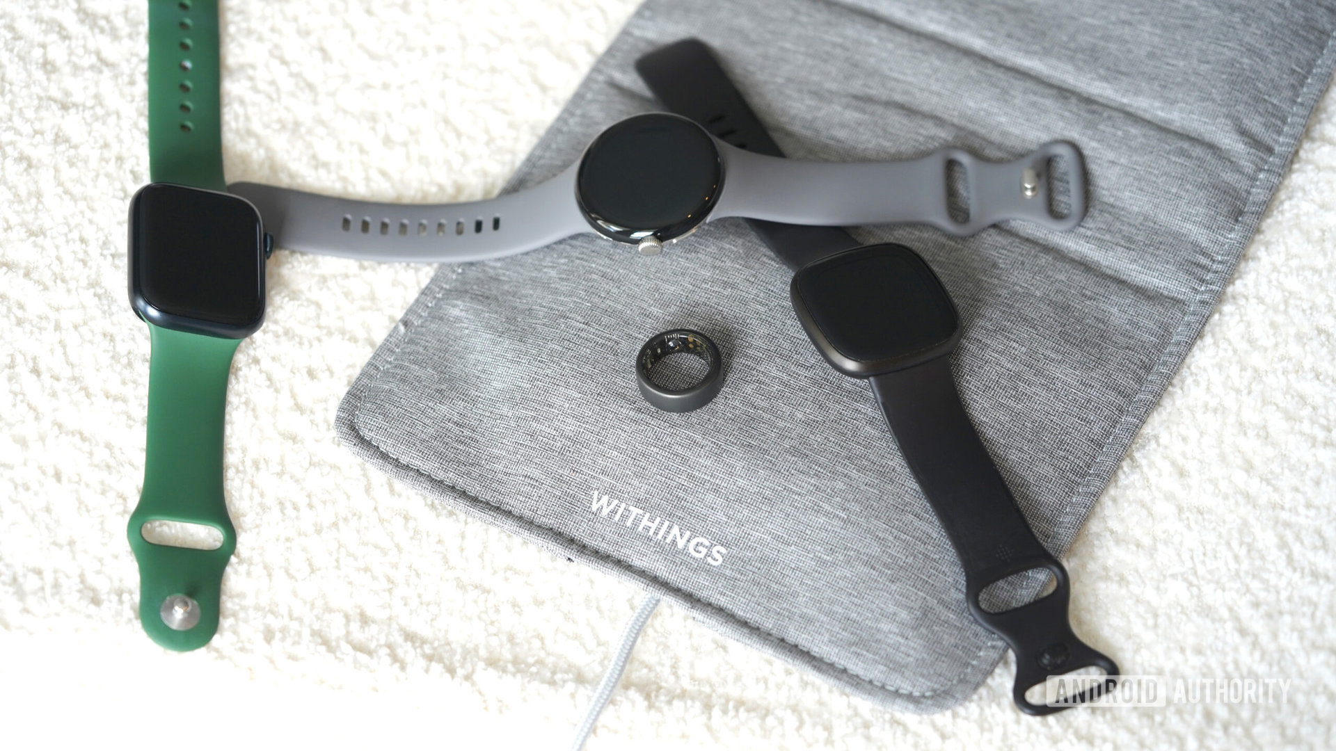 A variety of sleep tracking devices, including the Withings Sleep tracking mat, rest on a cozy boucle bench.