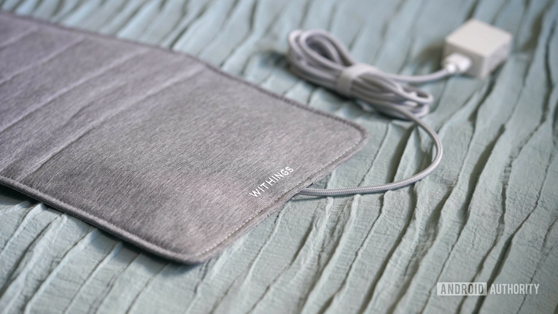 A Withings Sleep Tracking Mat rests on a sage comforter.