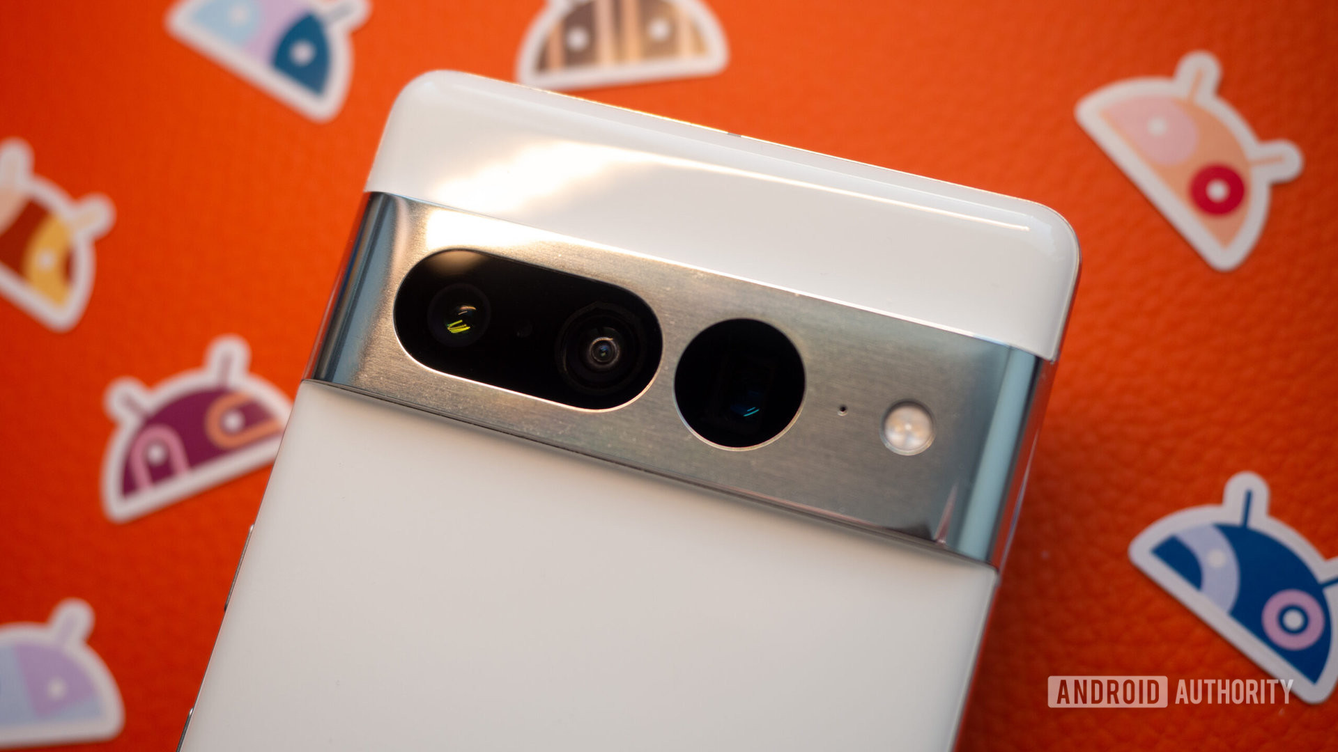 Google Pixel 7 Pro in white, focus on camera bump, on an orange background with Android stickers next to it