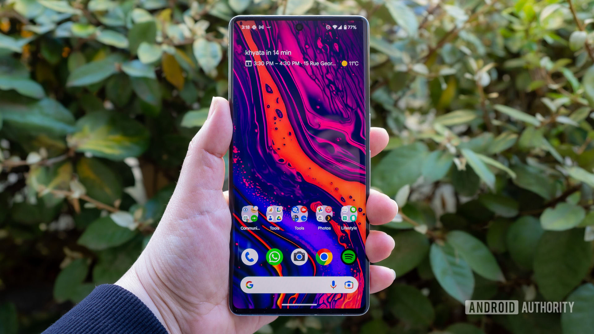 Google Pixel 7 Pro en la mano que muestra una pantalla de inicio brillante con arbustos verdes de fondo