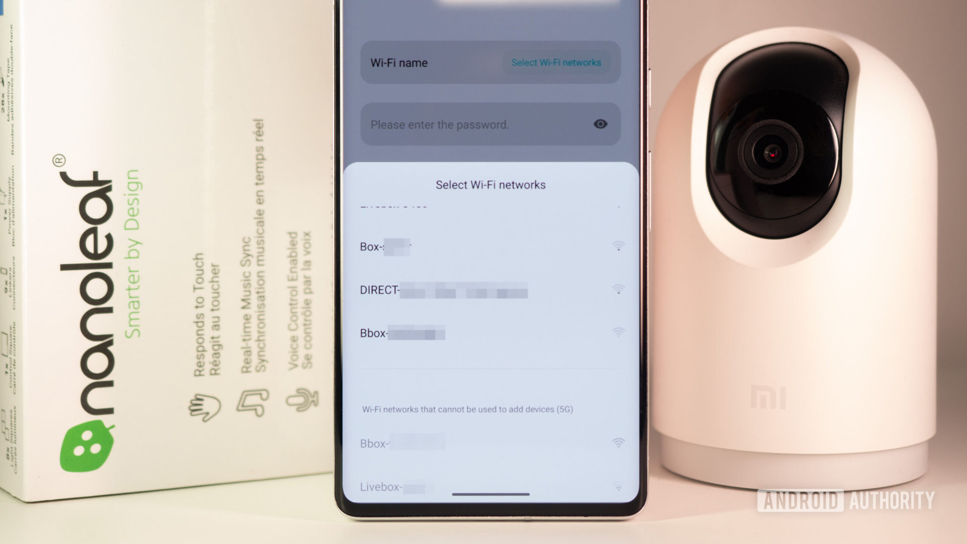 Xiaomi Mi 360 security camera and Nanoleaf Canvas box behind a smartphone showing an error when connecting to a 5GHz Wi-Fi network.