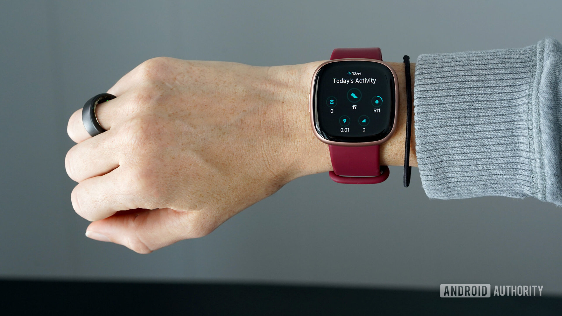A wrist wears a Fitbit Versa 4 with an Oura Ring 3 on the same hand.