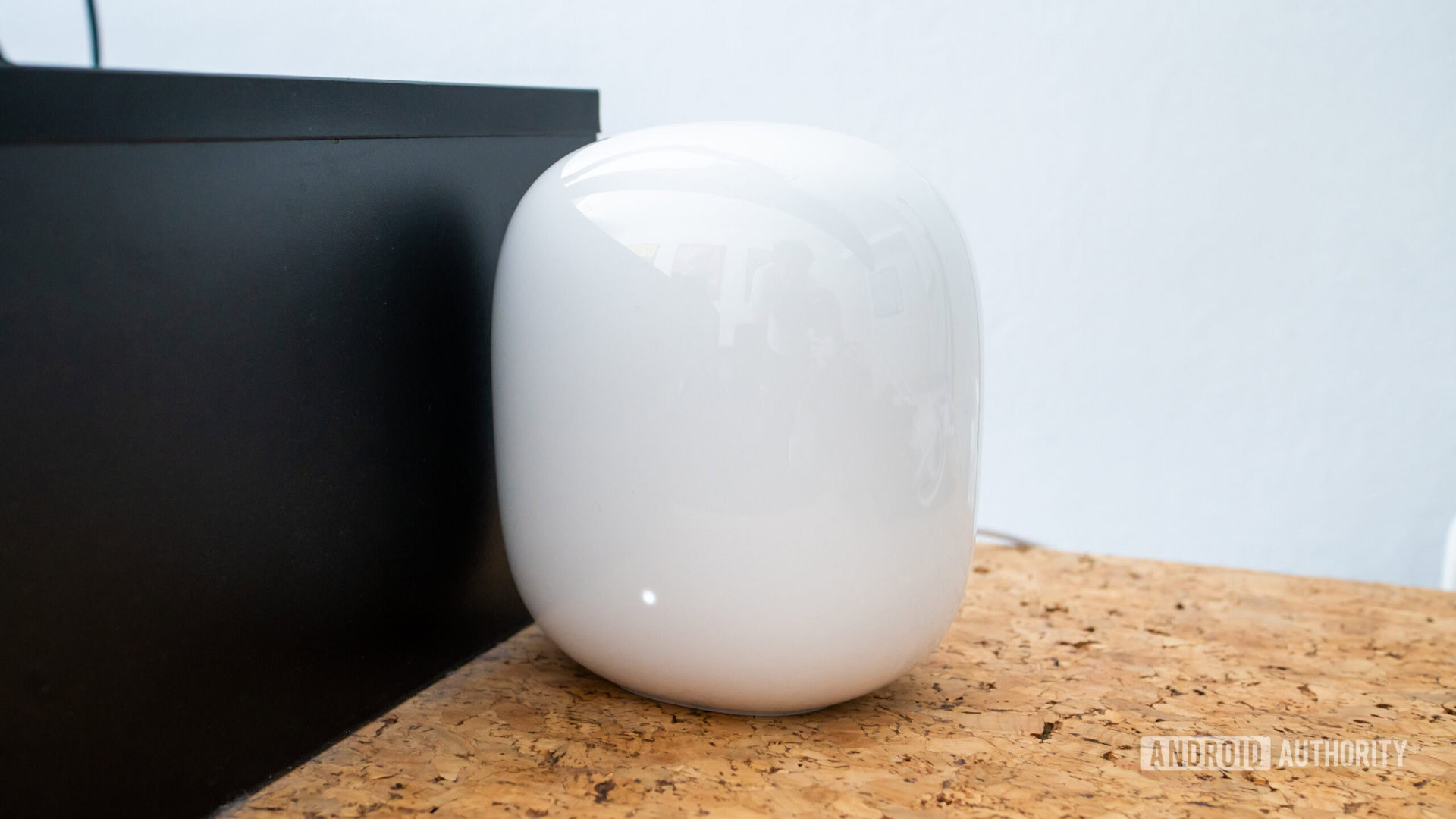 Google Nest Wi Fi Pro node on cork desk next to black wooden monitor stand