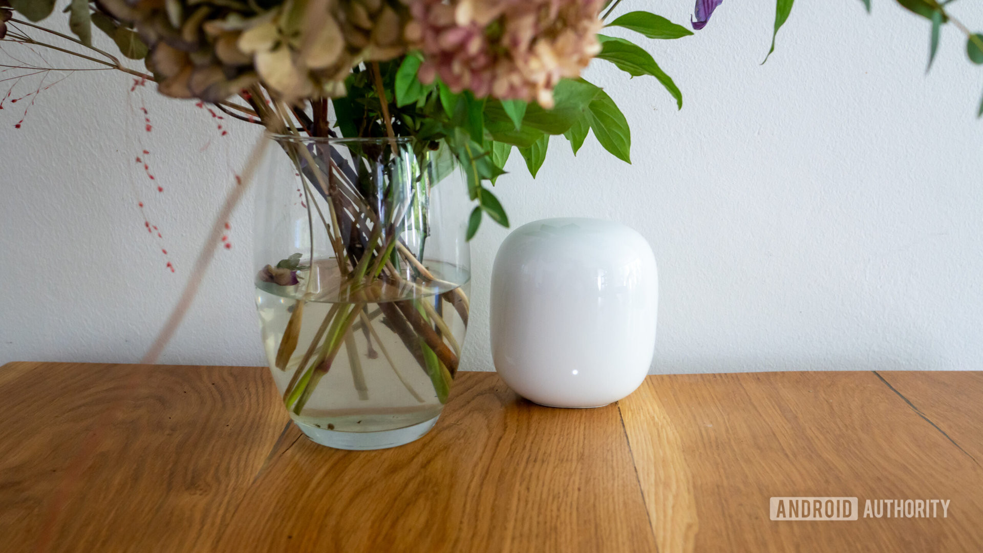 Tampilan depan router Google Nest Wi Fi Pro di atas meja di samping vas bunga