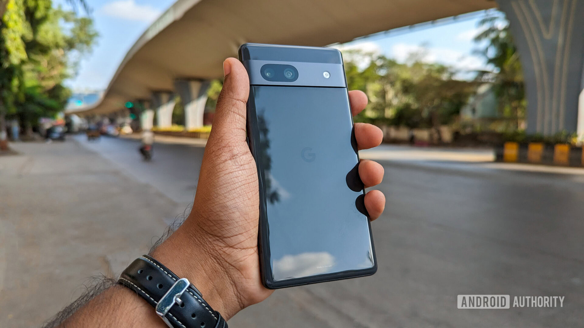 Google Pixel 7a en la mano, con una calle de la ciudad y un puente al fondo