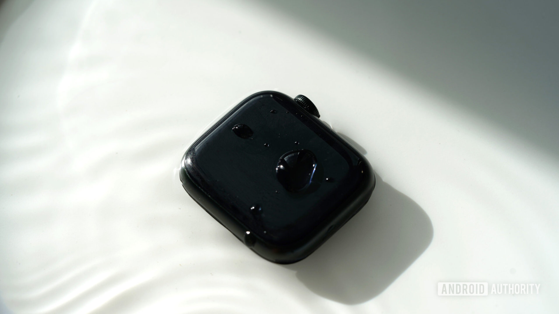 An Apple Watch Series 7 rests in a pool of water with drops on the watch case.