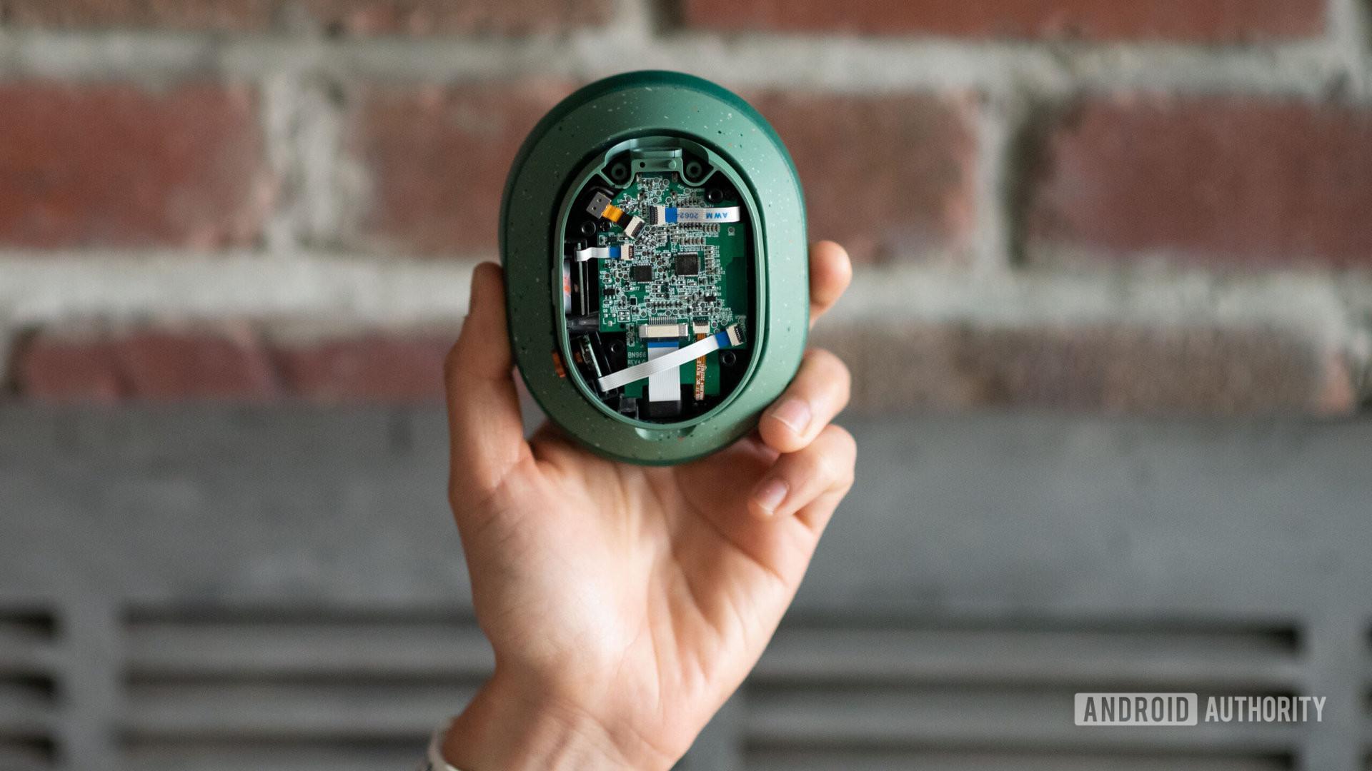 A hand holds up the Fairphone Fairbuds XL right ear cup module with the PCB in view.