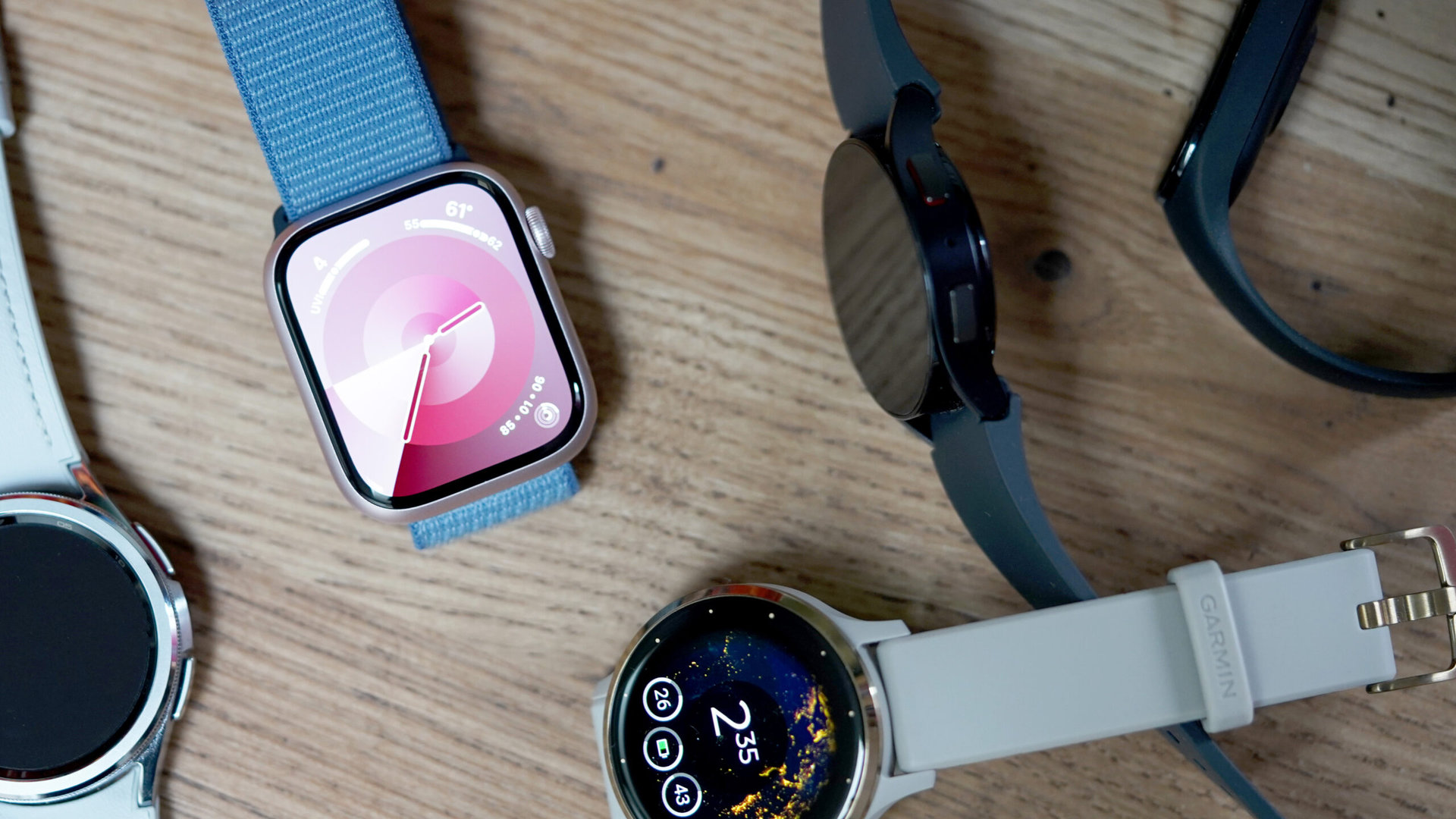 A variety of wearables rest on a wooden surface, representing the best smartwatches and trackers for women.