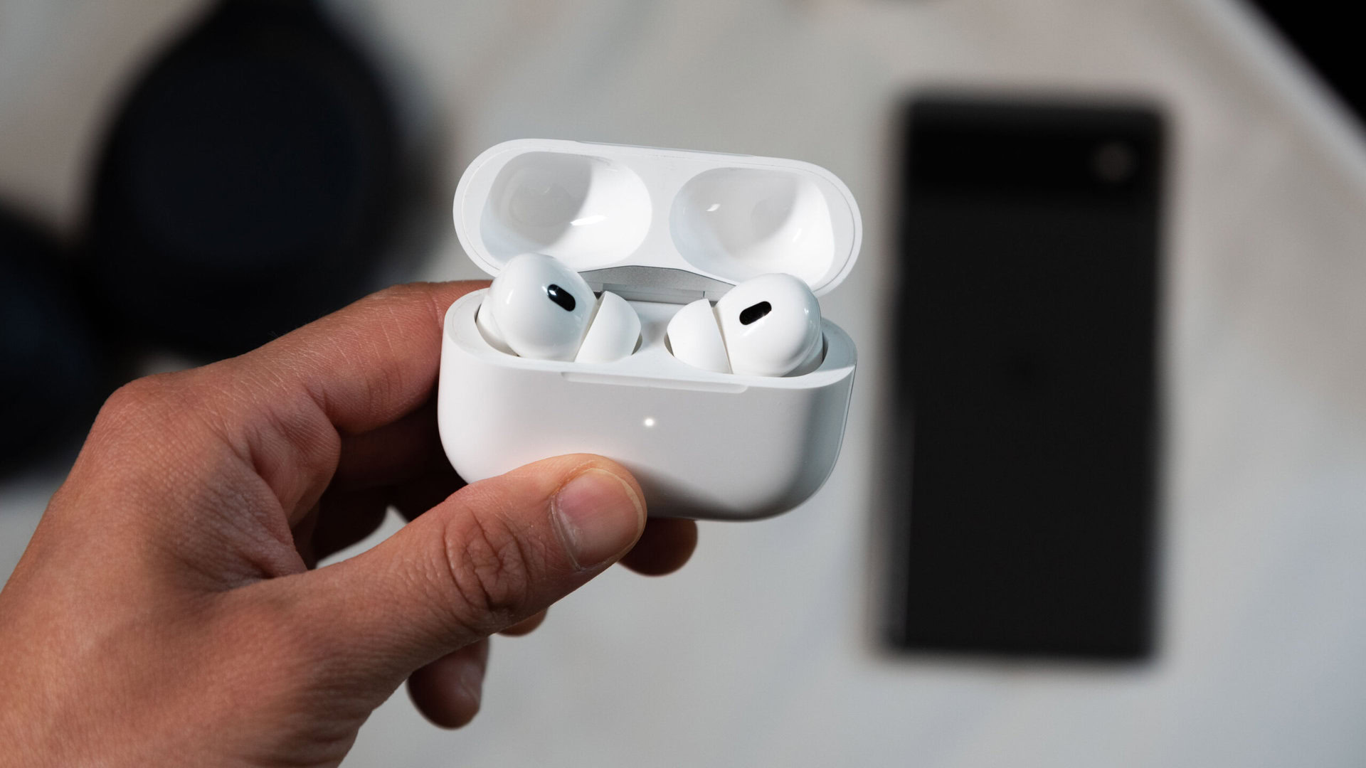 Una mano sostiene los AirPods Pro de segunda generación mientras está en modo de emparejamiento frente a un teléfono Pixel 6.