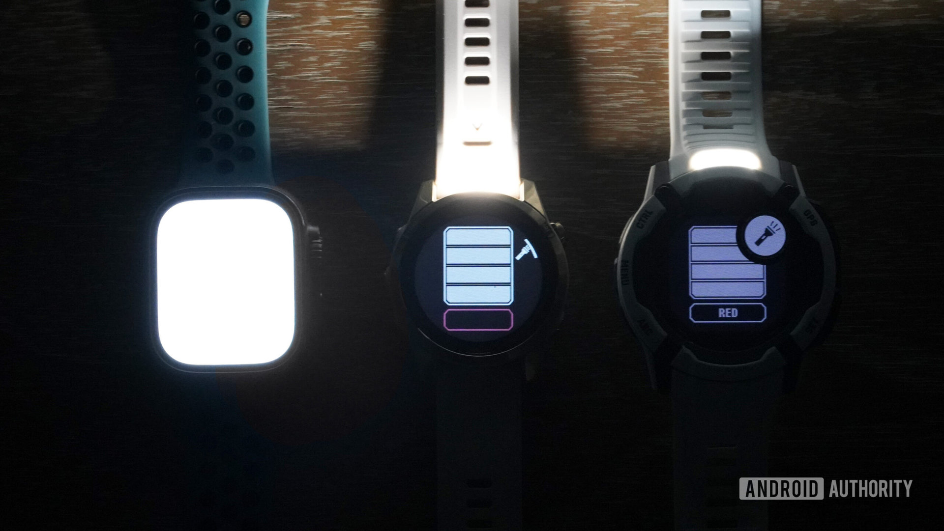 An Apple Watch Ultra rests alongside two Garmin devices, all with their respective flashlights enabled.