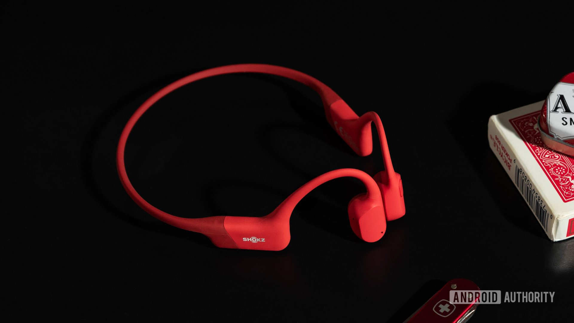 The Shokz OpenRun bone conduction headphones in red on a black surface.