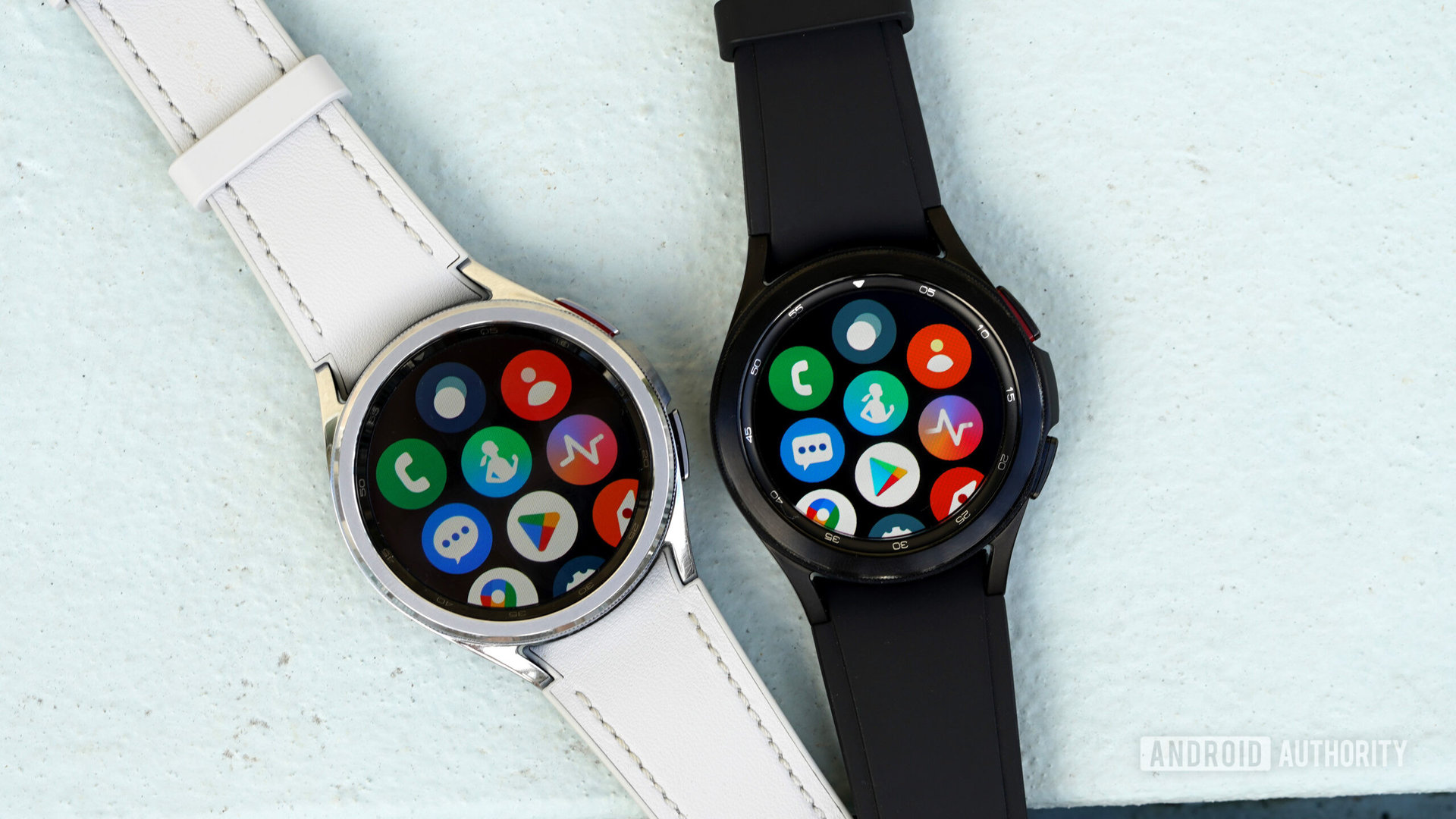 The most recent generations of Samsung Galaxy Watch Classics rest on a blue surface.