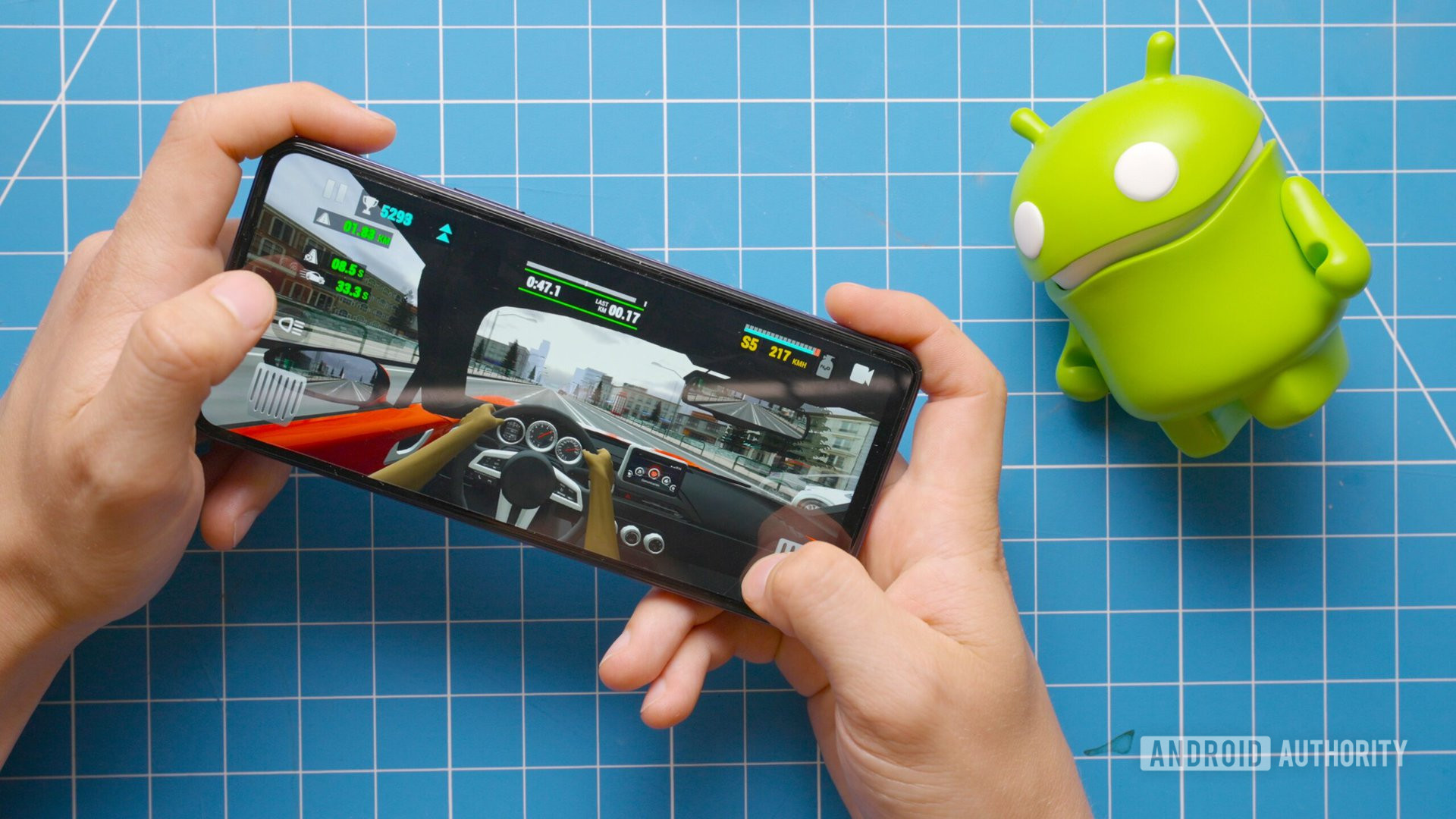 Playing Racing Limits on the Tecno Pova 5 Pro next to Android figure