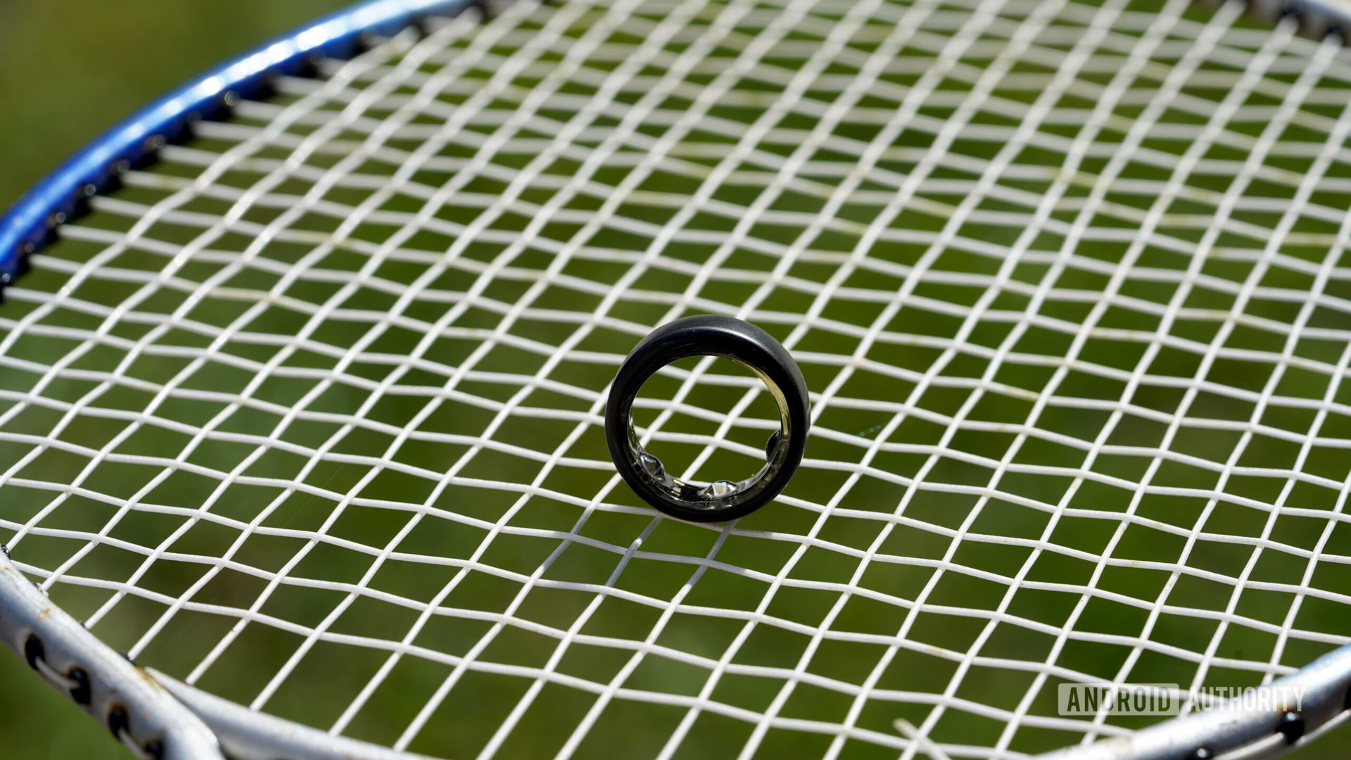 An Oura Ring 3 stands upright on a badminton racket.