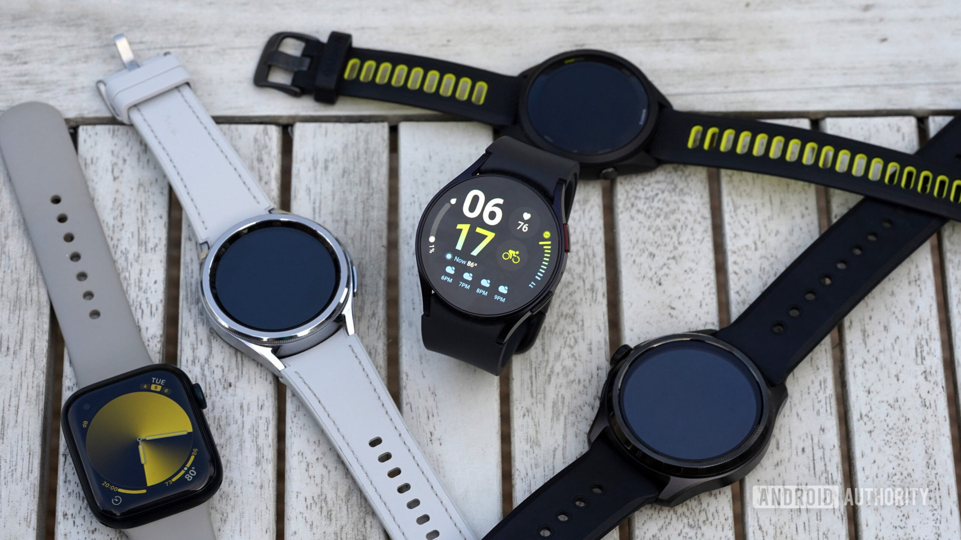A variety of leading wearables from Samsung, Apple, Garmin, and Mobvoi rest on a wood surface.