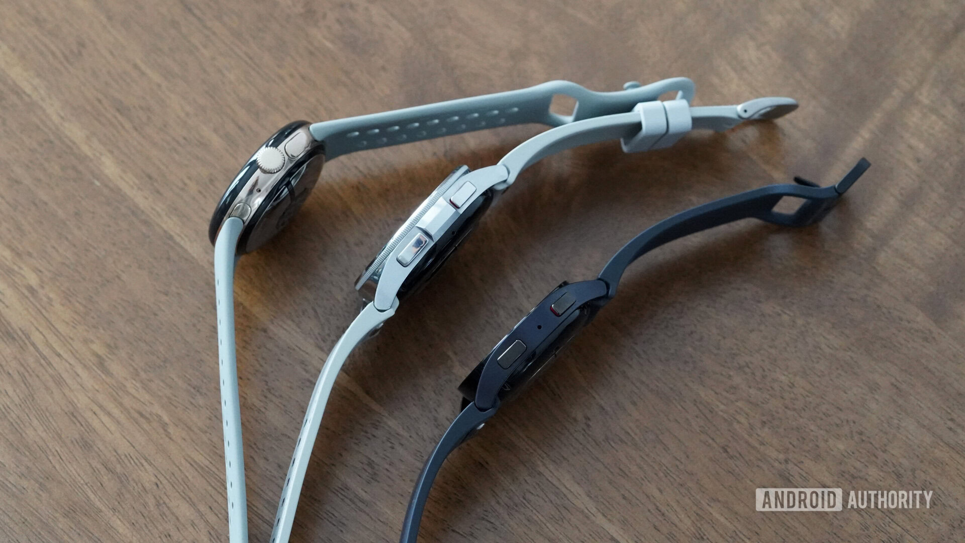 A Galaxy Watch 6, 6 Classic, and Pixel Watch 2 rest on their sides highlighting their contrasting designs.