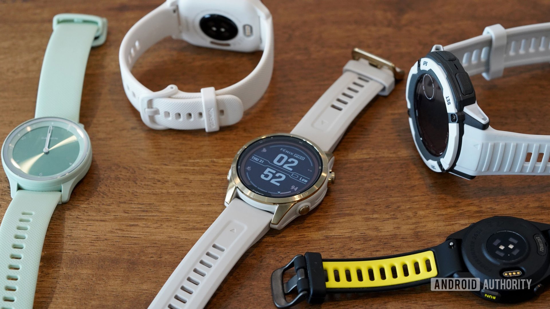 A variety of Garmin wearables rest on a wooden surface.