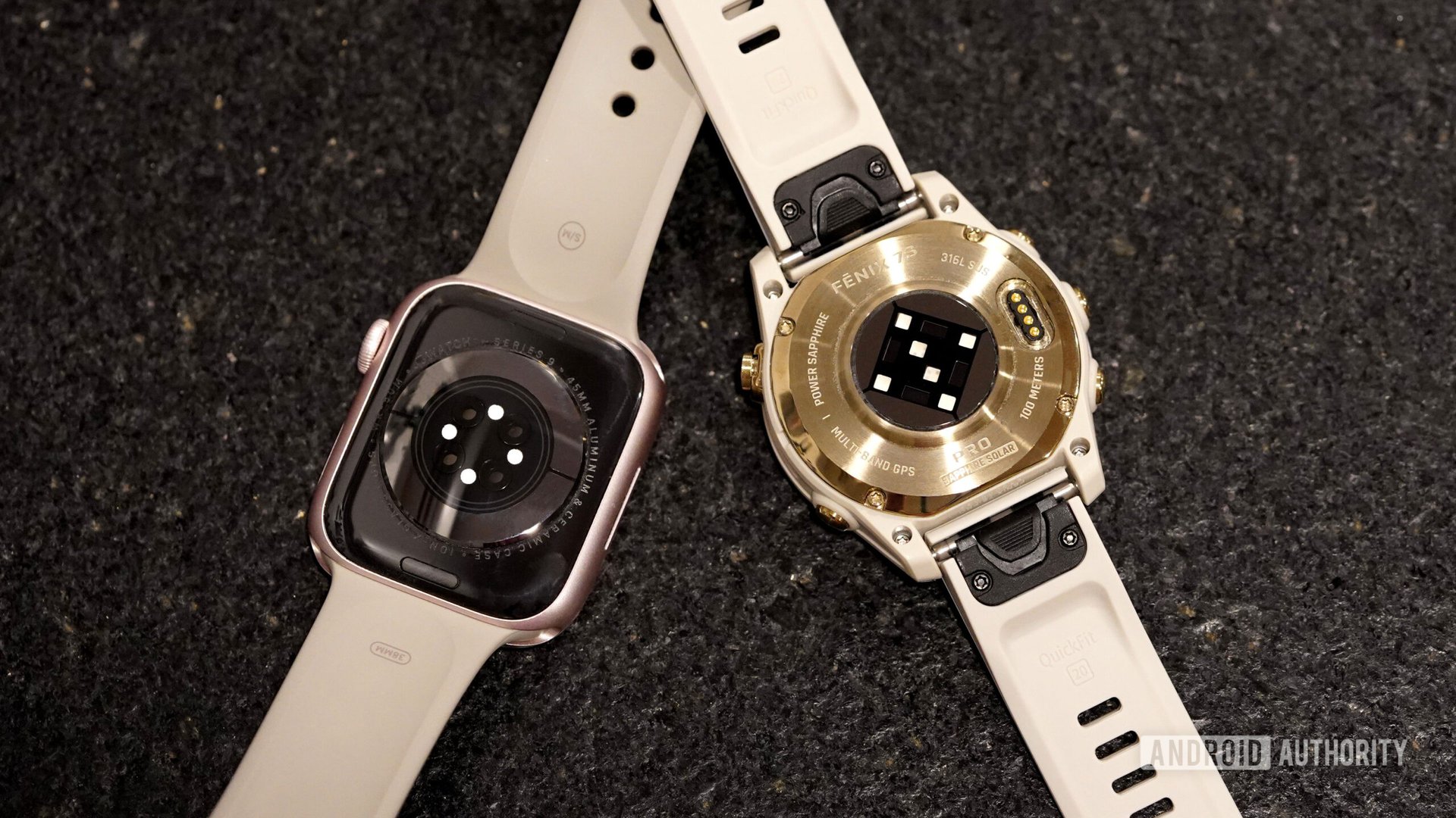 An Apple Watch Series 9 and Garmin Fenix 7 Pro rest face down, displaying their heart rate sensors.