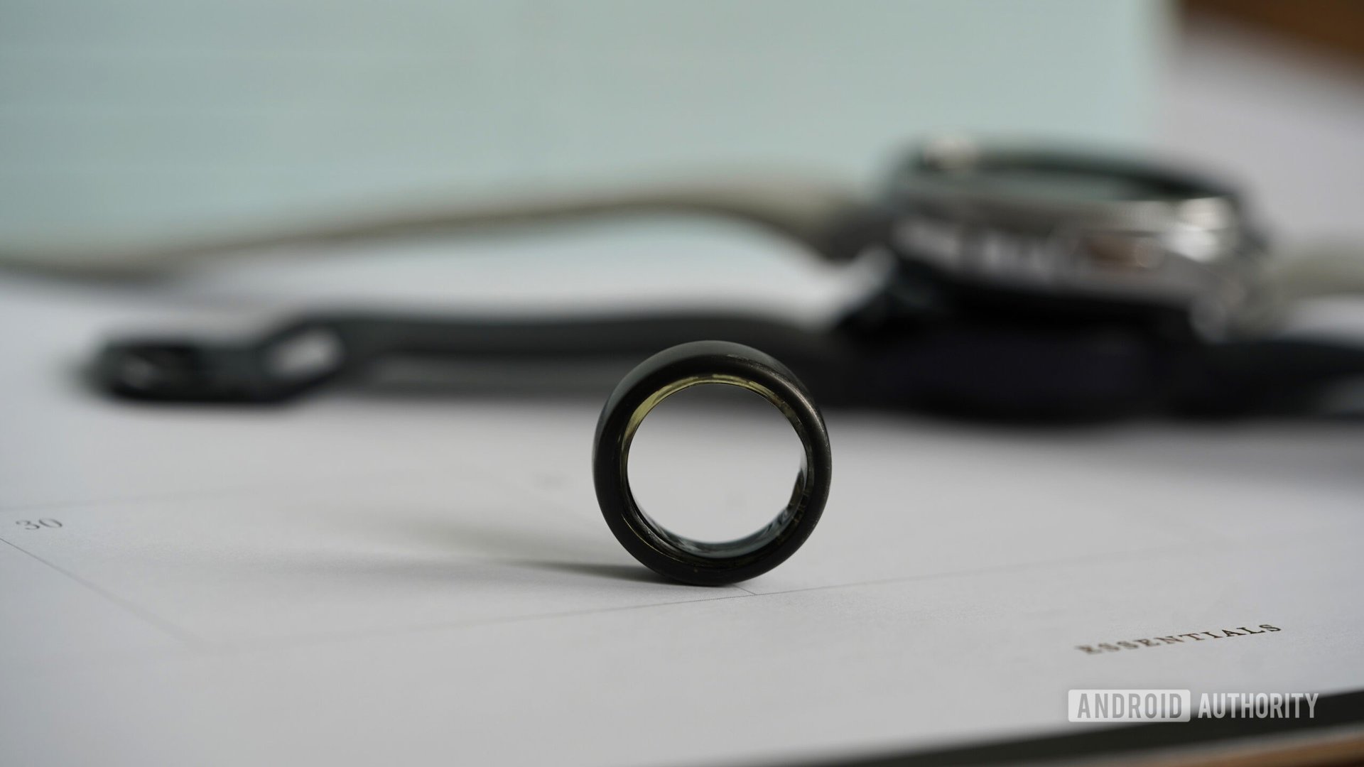 A smart ring rests in front of a variety of Samsung Galaxy Watches.