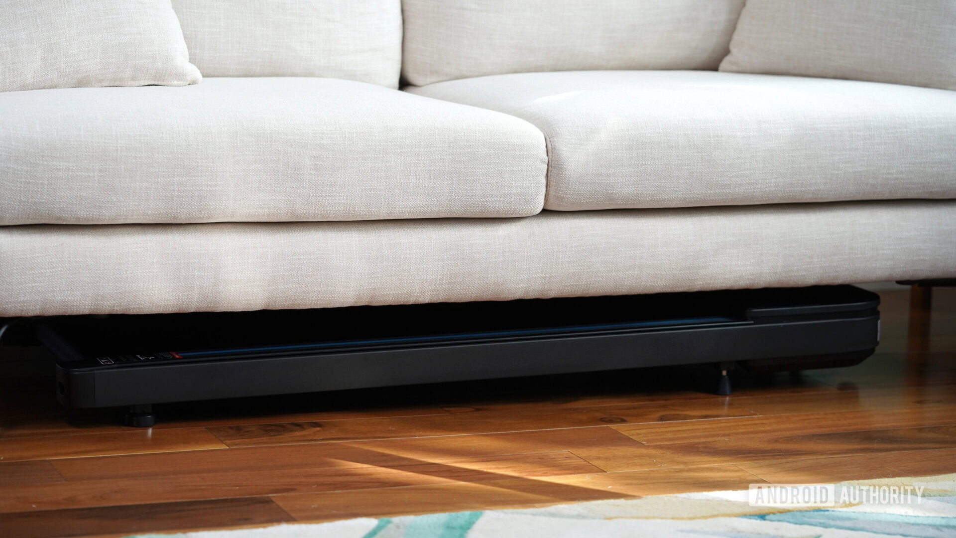 A Mobvoi Home Walking Treadmill is stored under a small couch.