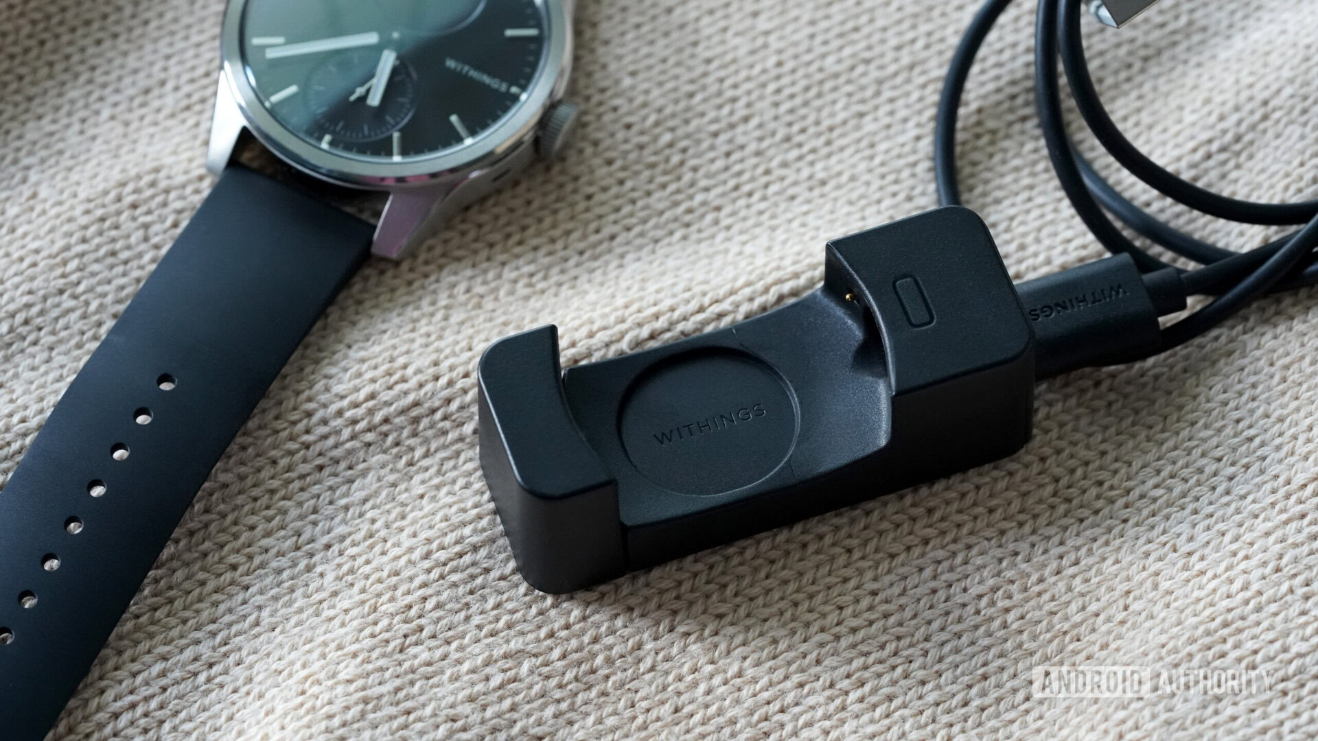 A Withings ScanWatch 2 charger rests along side the device.