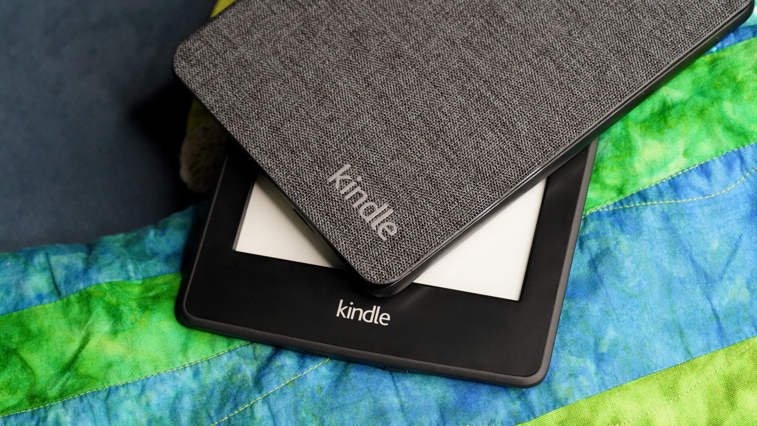Assorted Kindle models A pair of Kindles rest on a throw blanket.