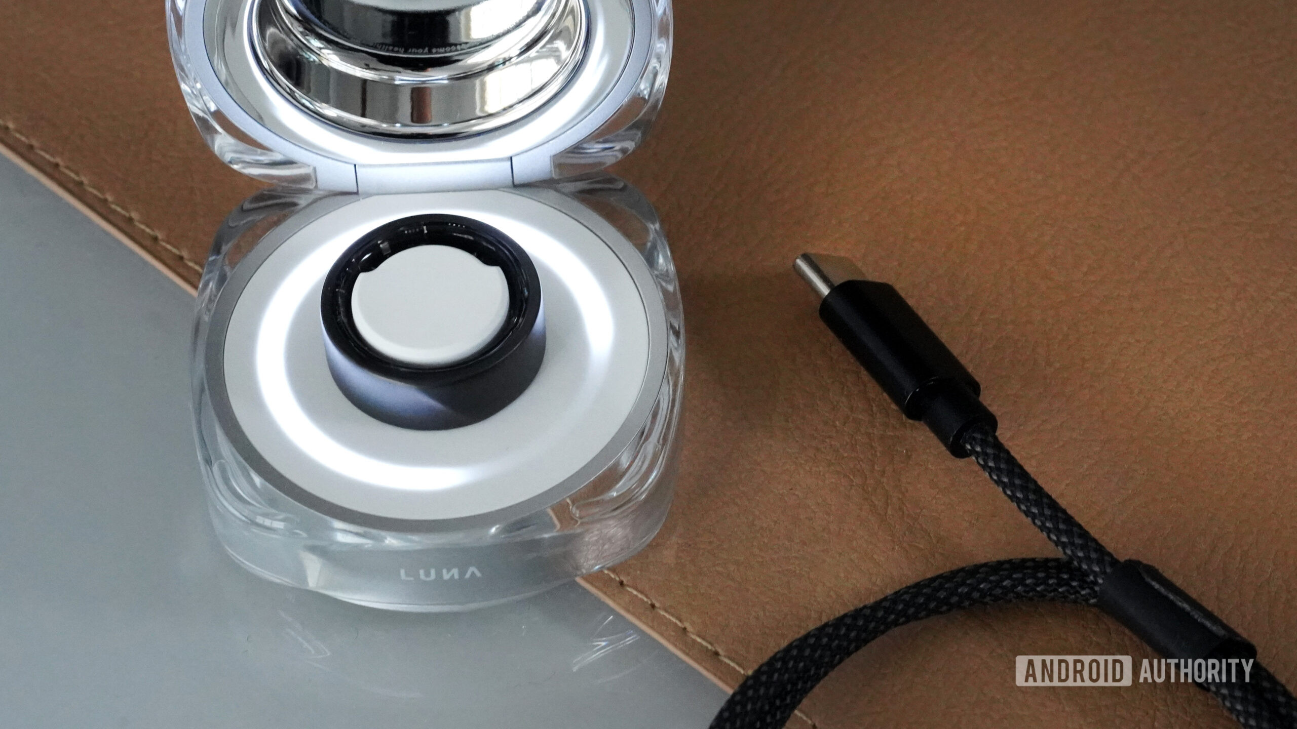 A Luna Ring 2 rests in its charger aongisde the USB-C cable