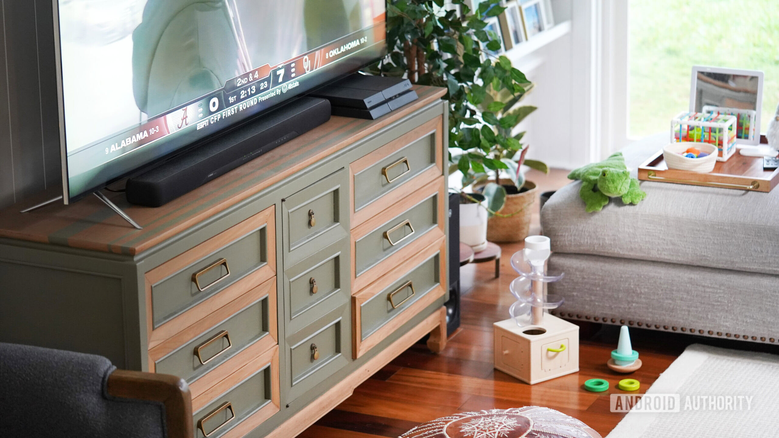 A living room set up includes an oversized TV, TV stand, and toddler toys.